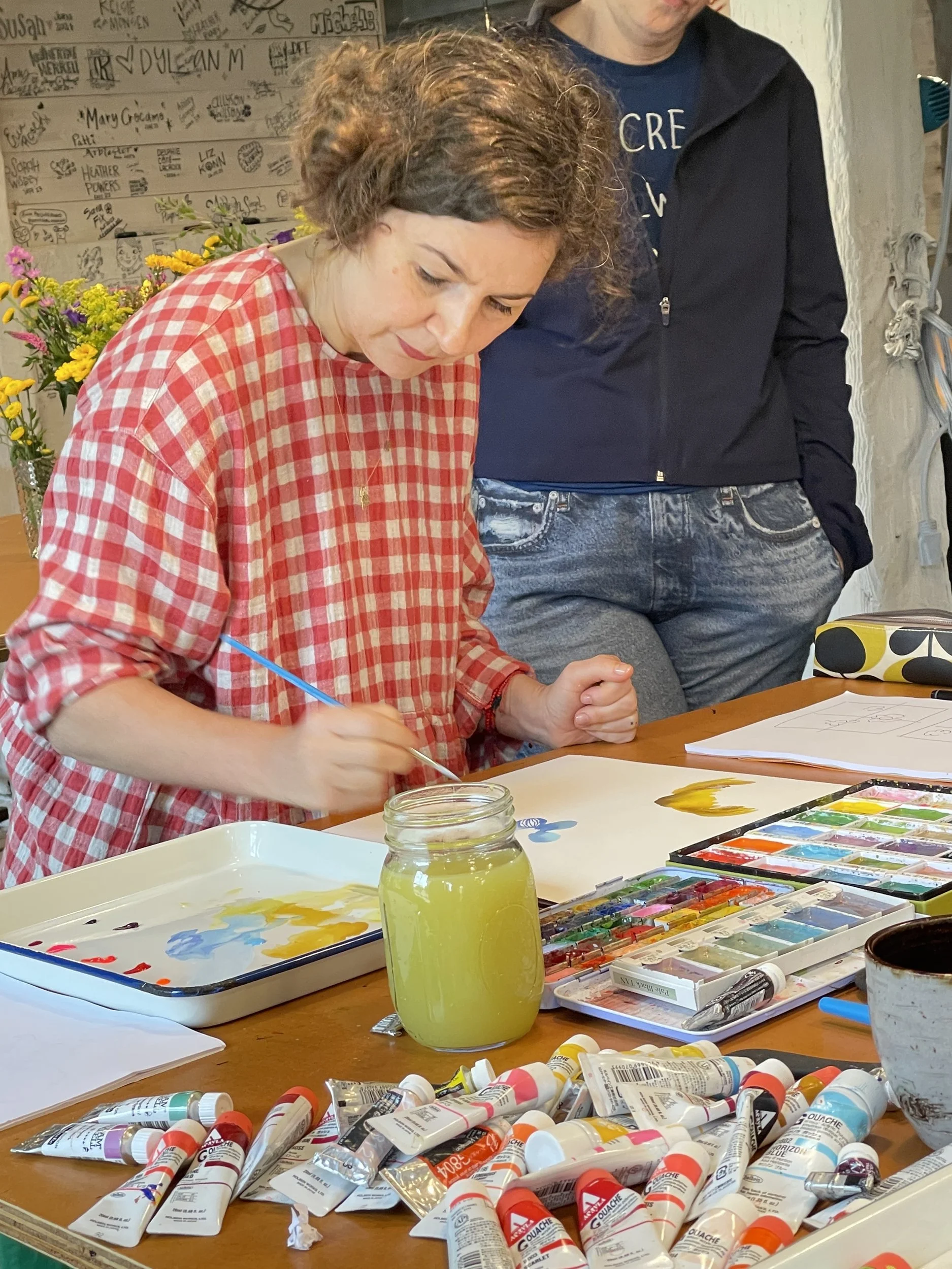 Helen Dardik painting florals at a table full of watercolor paints and tubes in the barn studio