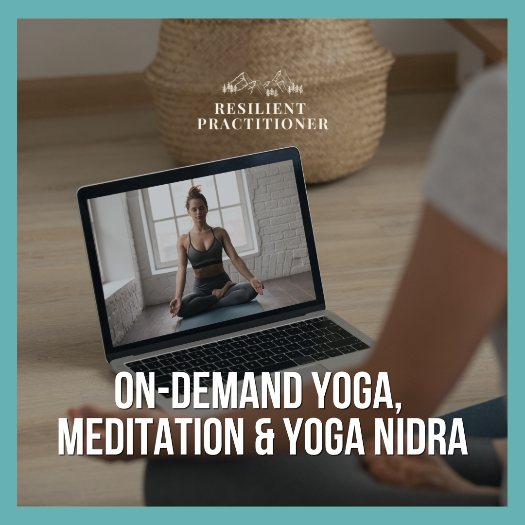 A person watching an online yoga class on a laptop, with a woman in yoga attire seated in a meditation pose on the screen; the background shows a woven basket and a wooden floor.