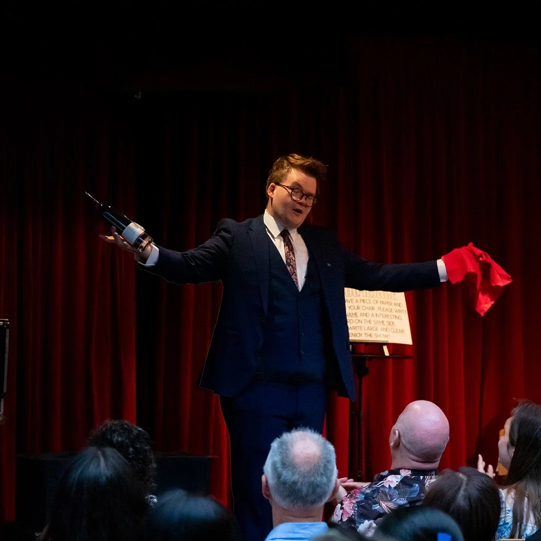 agical MC host Josh Staley on stage presenting a celebratory wine gift during a Melbourne event reception.