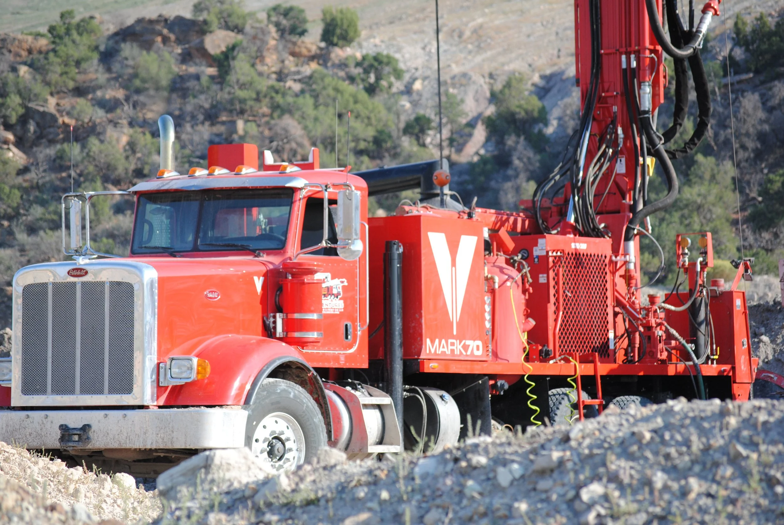 A red reverse circulation drilling machine is working in an active mine site.