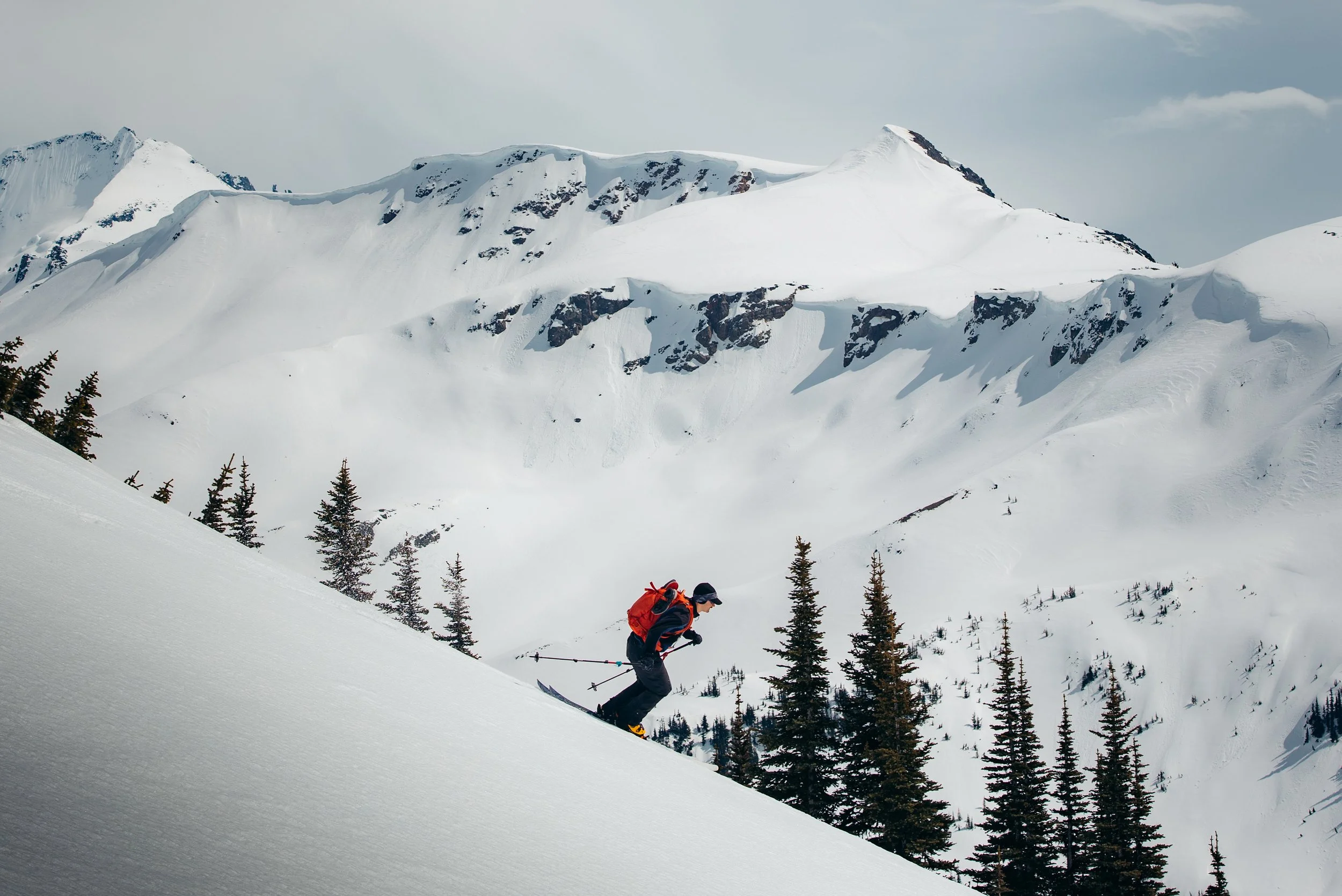 A person skiing down a snow-covered mountain slope surrounded by snow-capped peaks and evergreen trees.