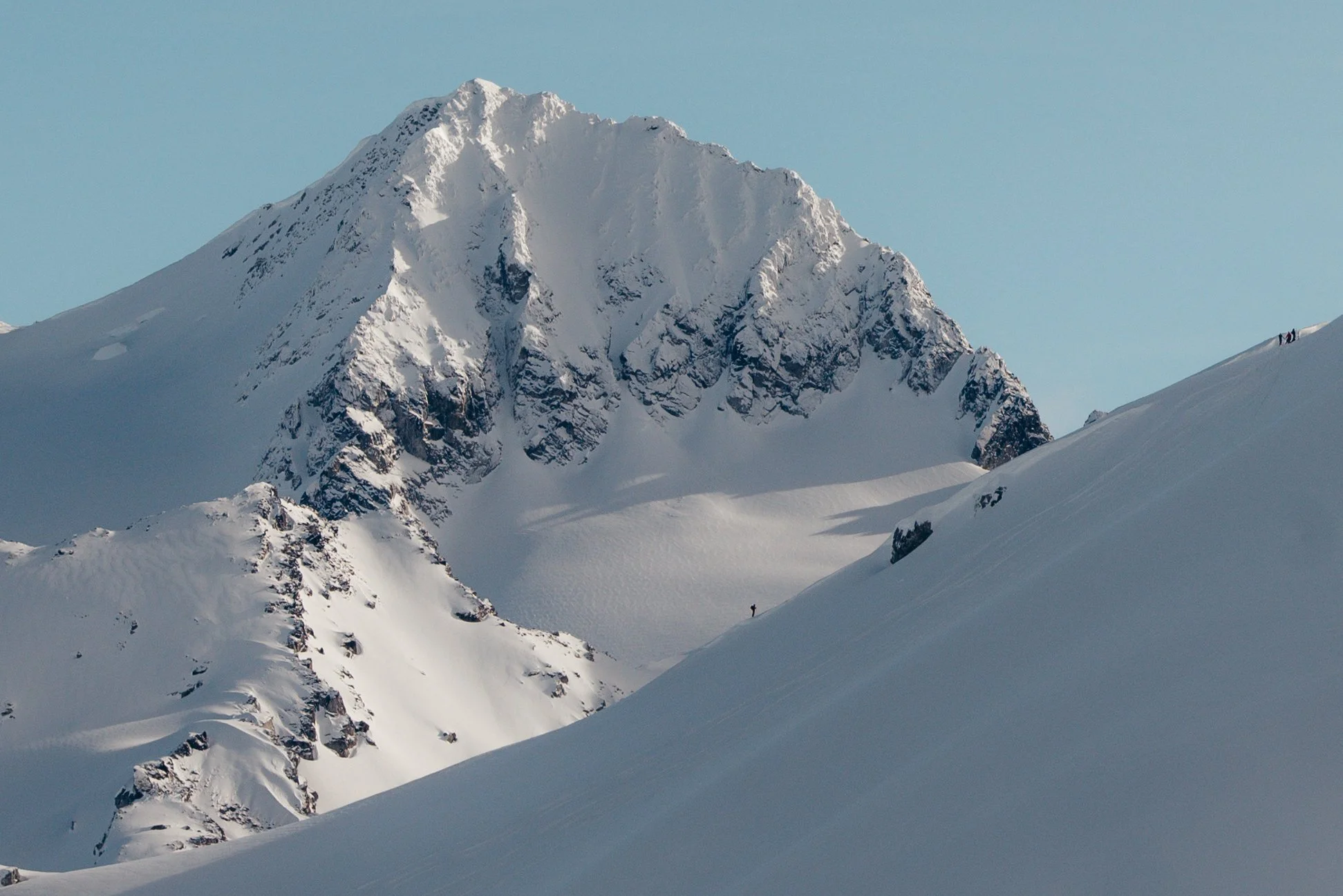 Snow-covered mountain peak with a few climbers visible near the top and on the slope.