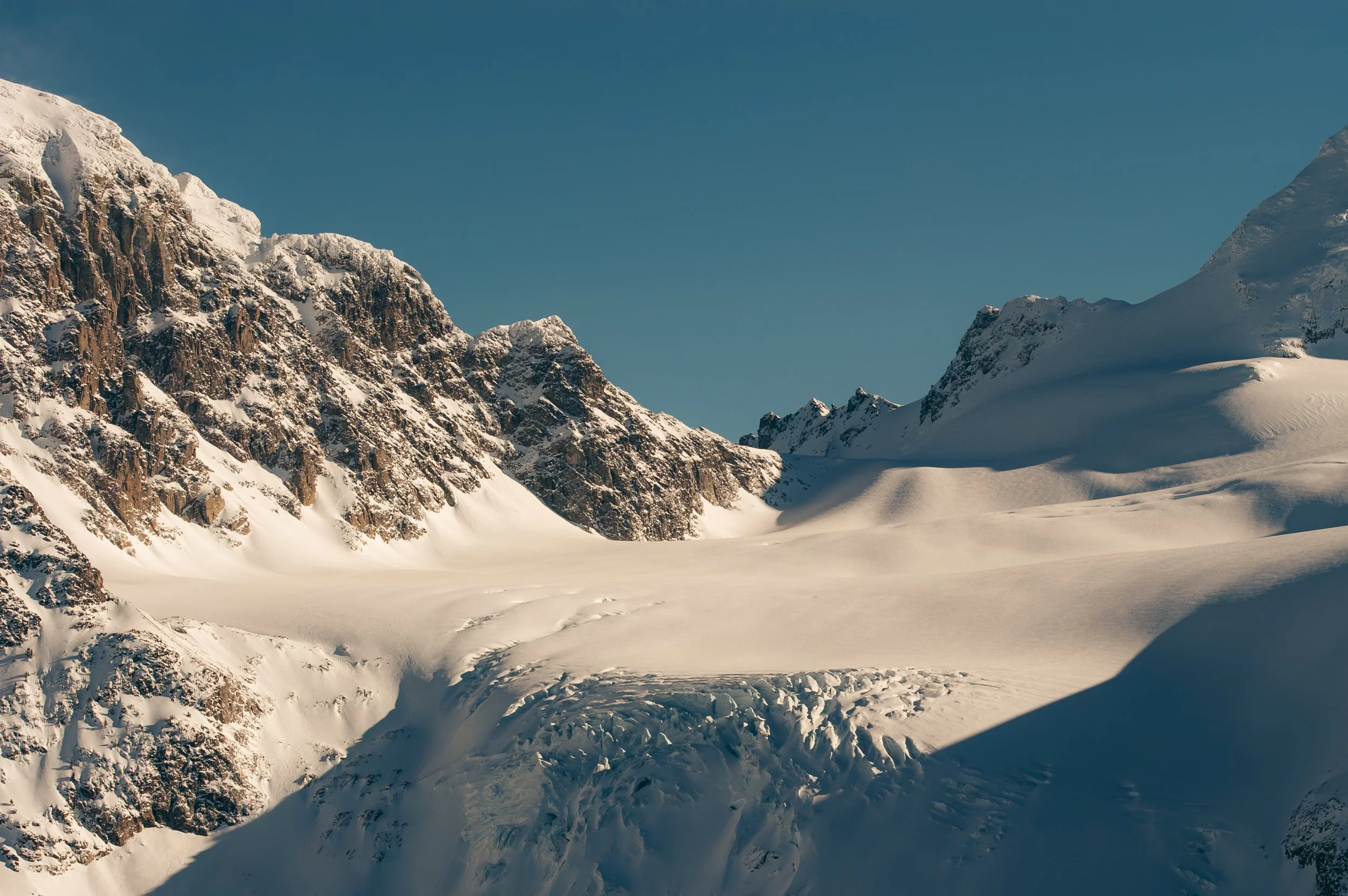 Snow-covered mountain valley with rocky peaks and clear blue sky.