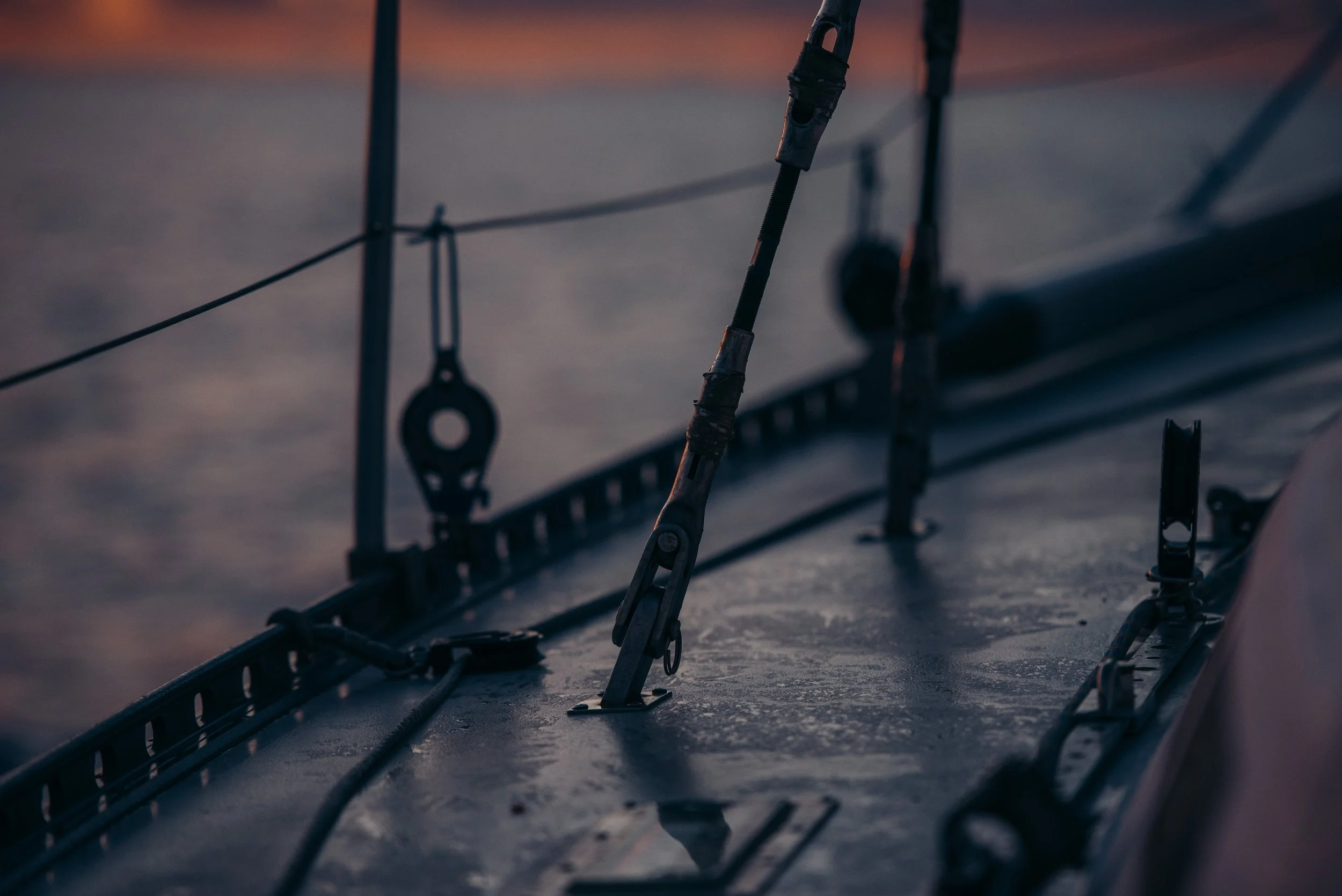 Close-up of a sailboat deck with rigging and hardware during sunset.