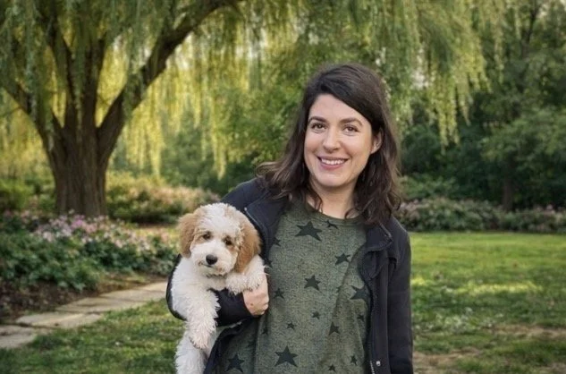Beautiful brown haired woman holding a happy dog outdoors in a grassy field.