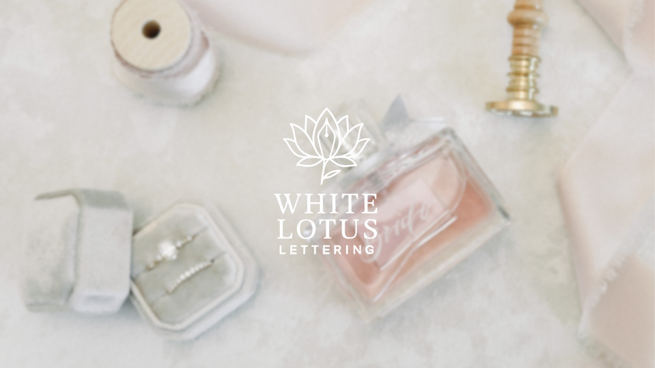 Flat lay of jewelry, perfume, and decorative objects on a light fabric surface, with a logo for White Lotus Lettering in the center.
