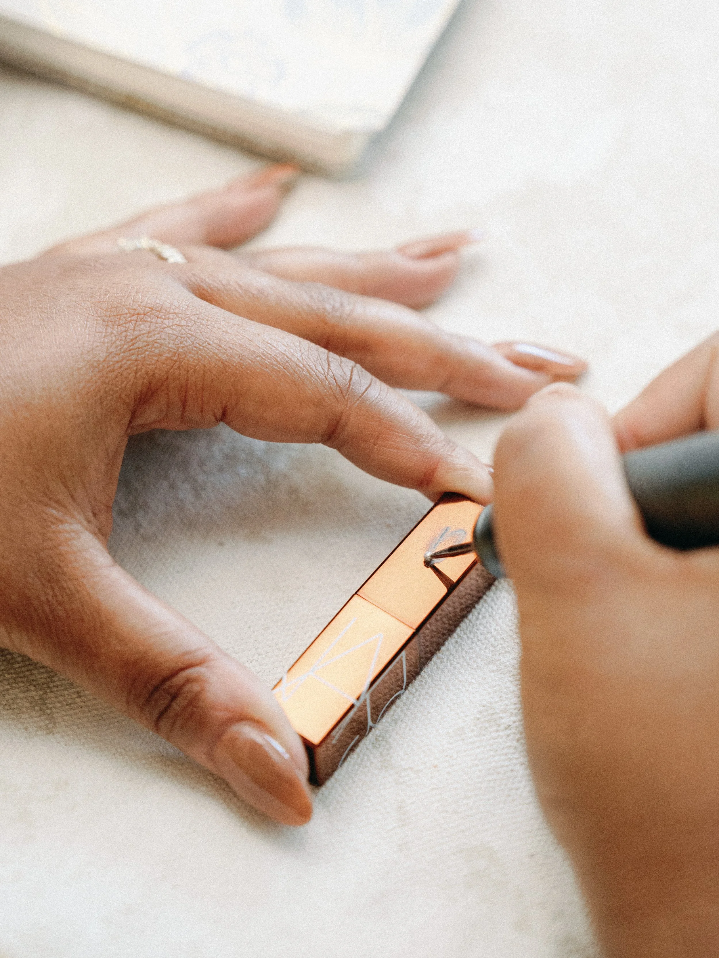 Person applying or testing makeup with a small makeup palette and a brush on a light-colored surface.