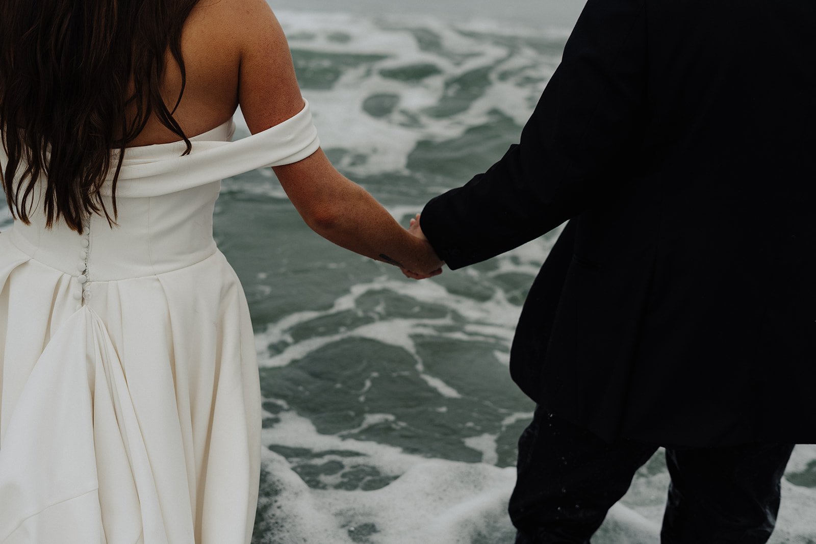 Bride and groom holding hands in the ocean