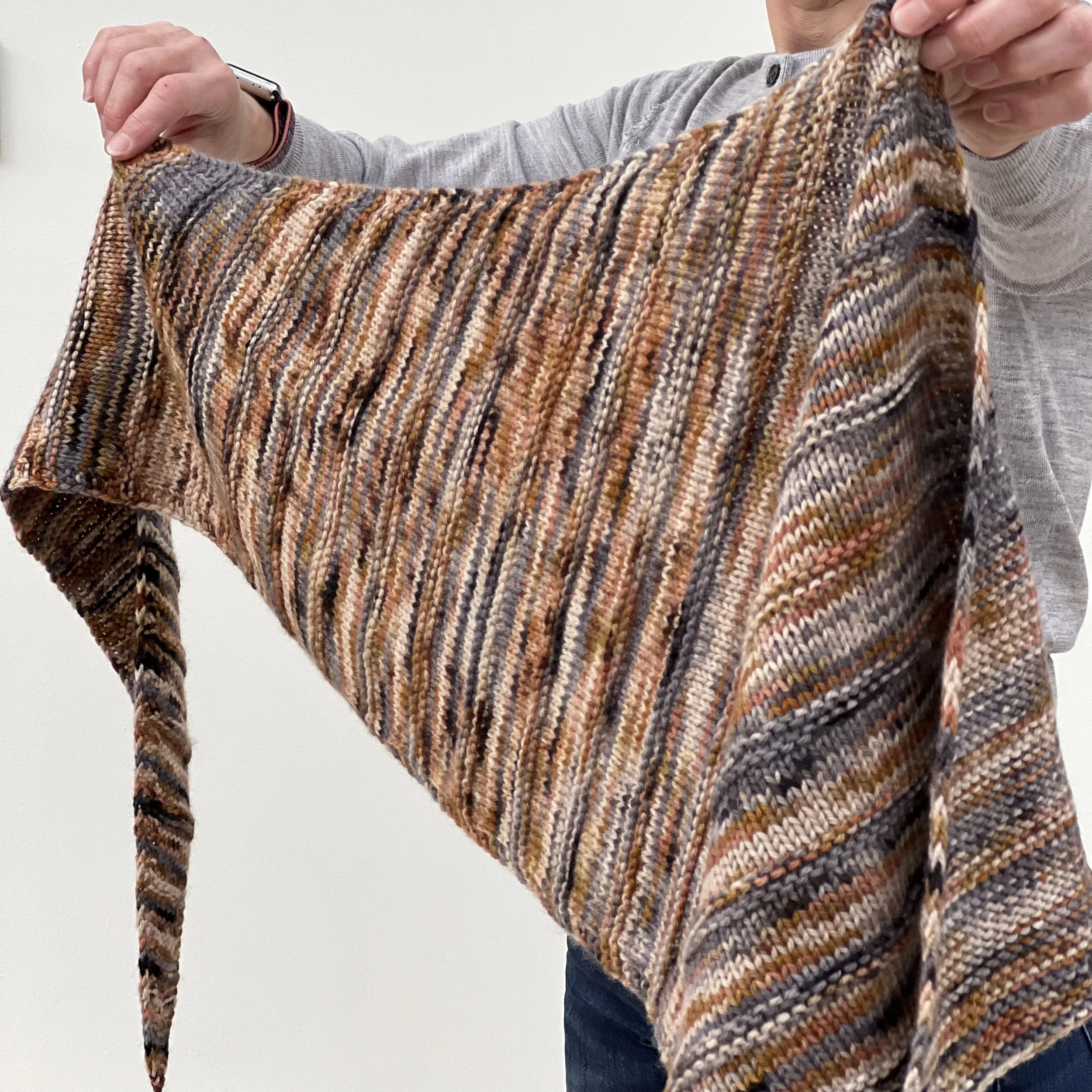 Emma is holding the Vega Shawl with two hands to show the length of the top edge of the shawl