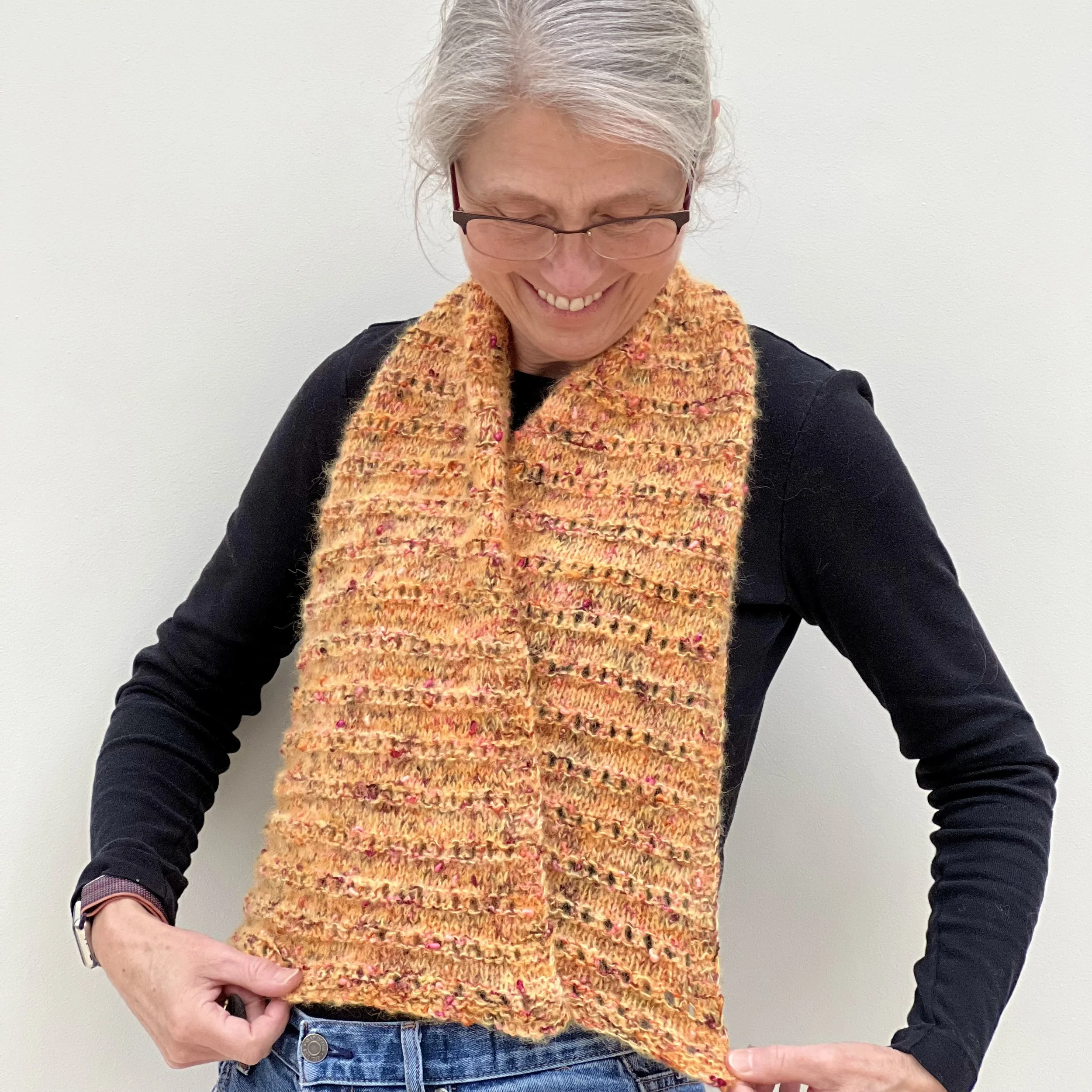 Emma is wearing the small knitted Parallel Lines Shawl and is holding both wide ends open to show the ridged eyelet stitch pattern