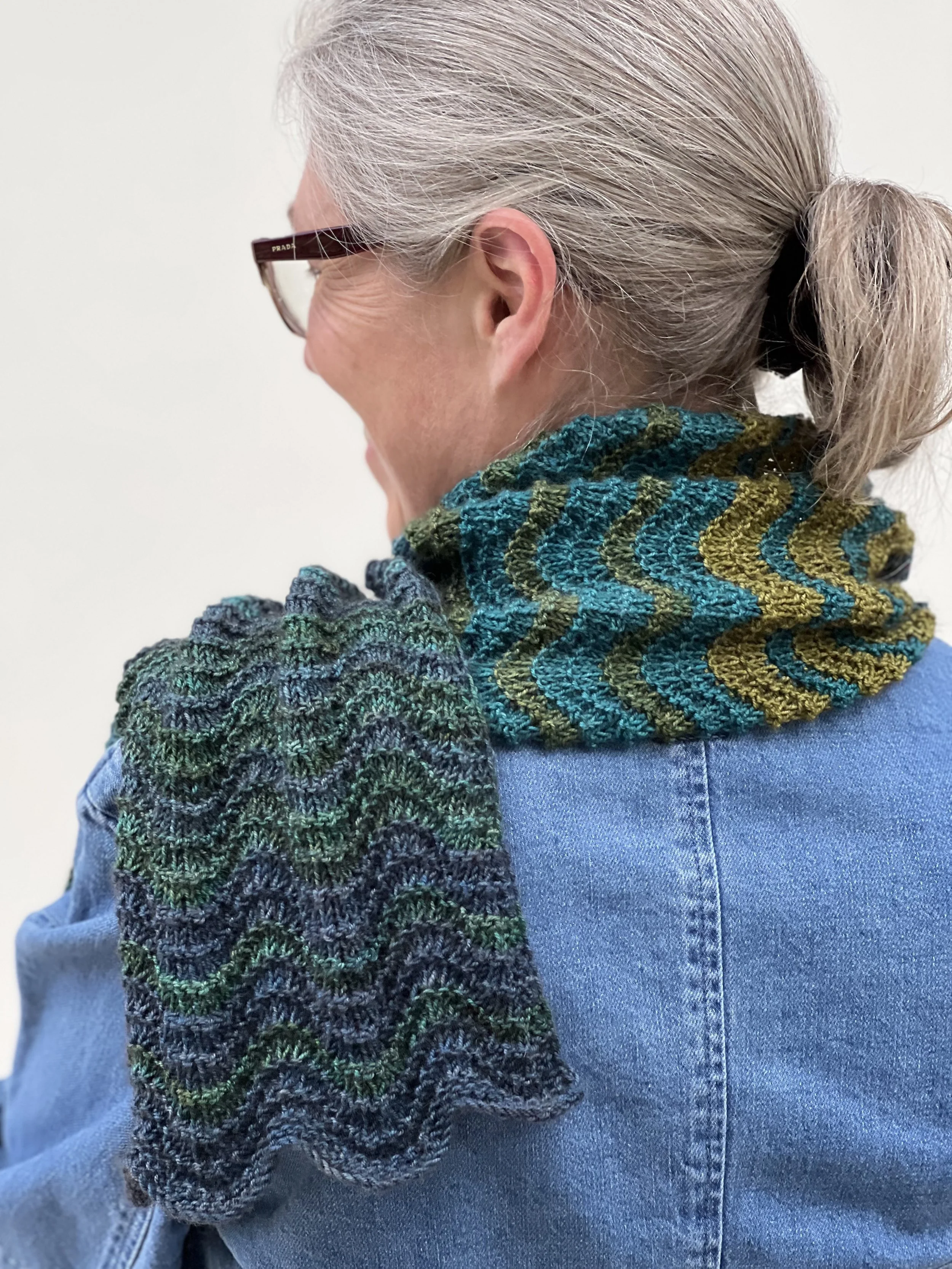 Emma is facing away from the camera to show the chevron pattern on the rolling waves shawl she is wearing draped over her shoulder.