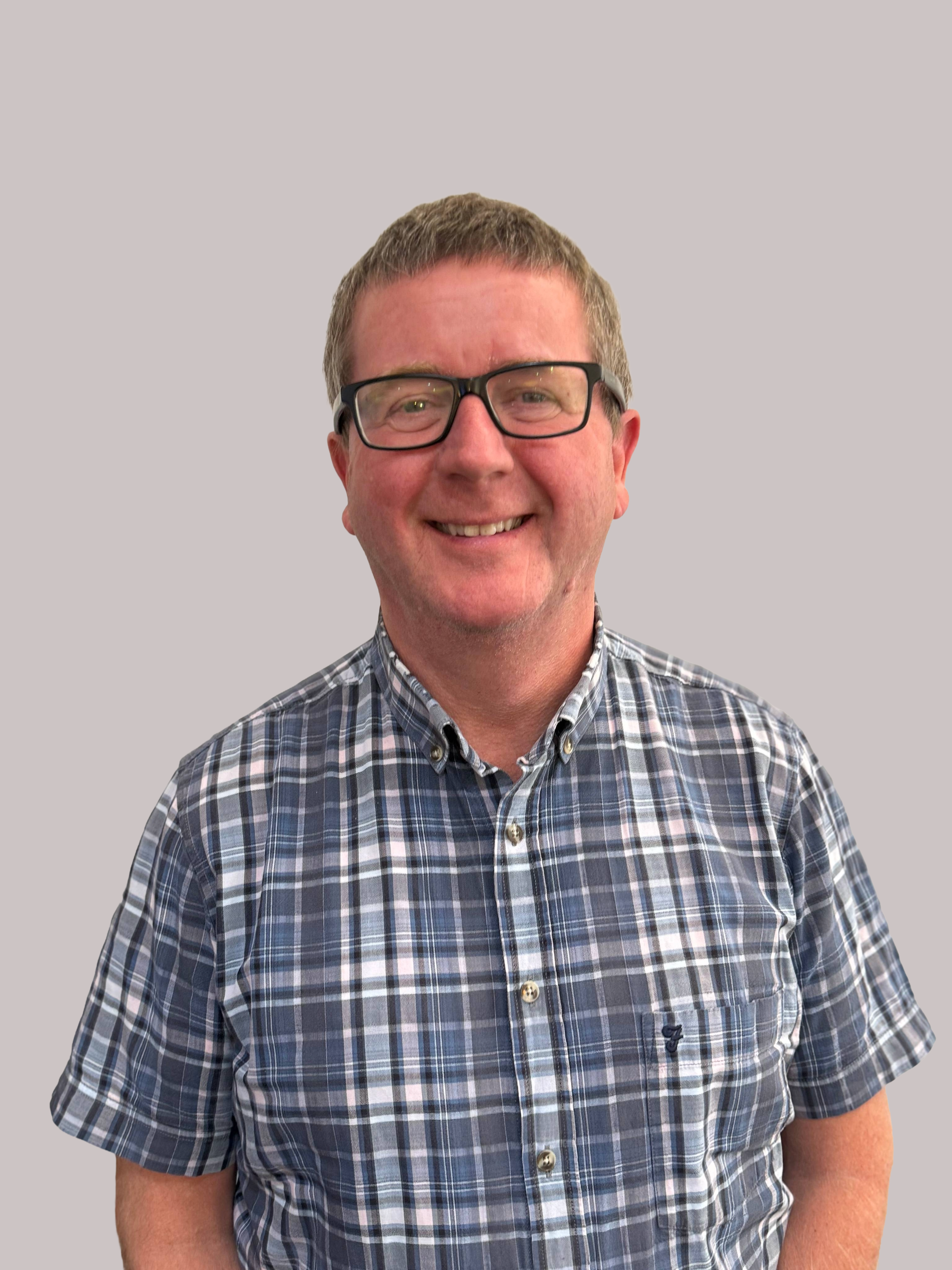 Man wearing glasses and checkered shirt, smiling on grey background