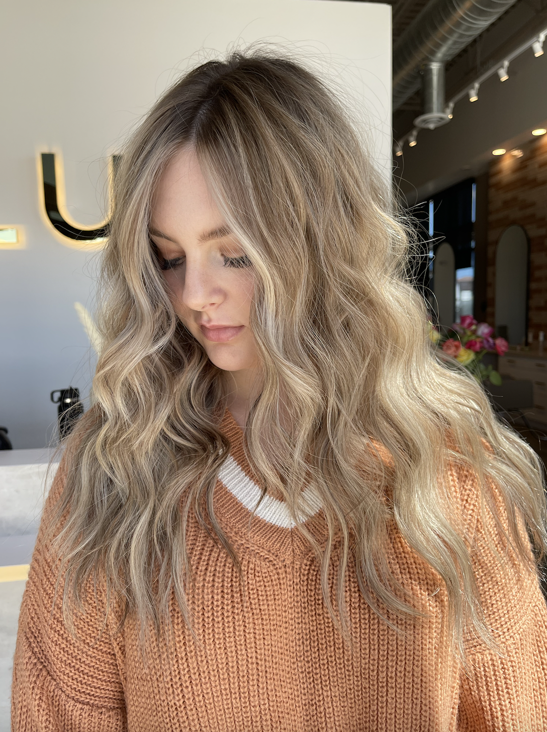 A woman with long, curly blonde hair looking down inside a modern cafe or restaurant.