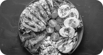 A black and white photograph of a plate with sliced eggs, cherry tomatoes, and what appears to be slices of bread or toast, garnished with herbs.