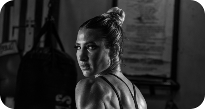 A black and white photo of Sydney with her hair in a bun, wearing a workout top, looking over her shoulder in a gym setting.