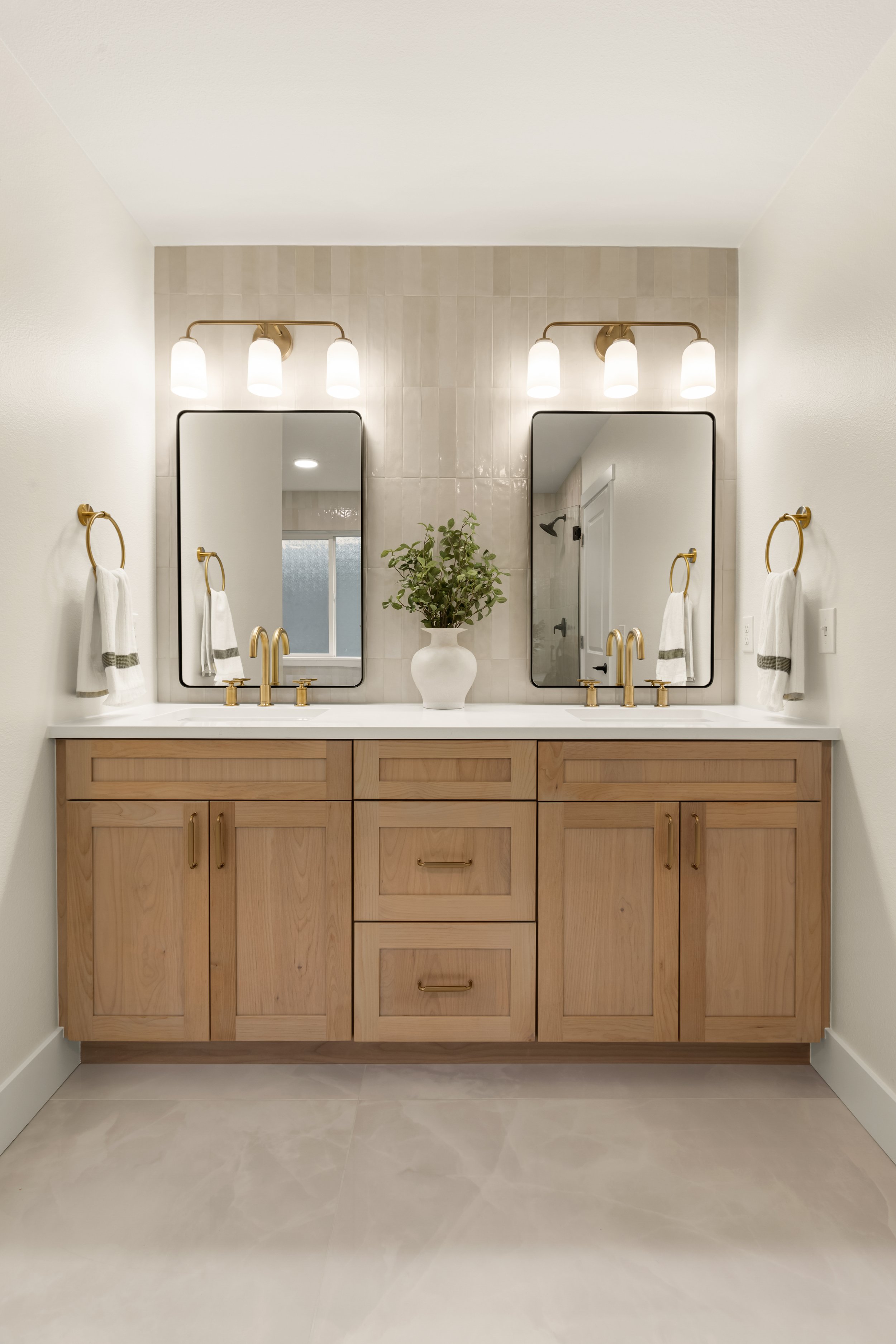 A modern bathroom vanity with two mirrors, gold fixtures, and a potted plant between the mirrors.