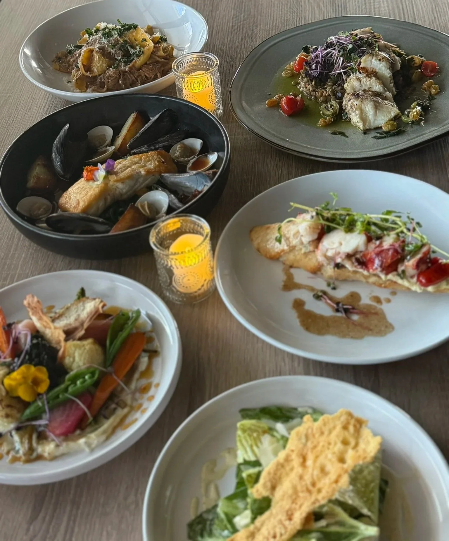 Assorted dishes of gourmet seafood and salads on a wooden table, with two lit candles.