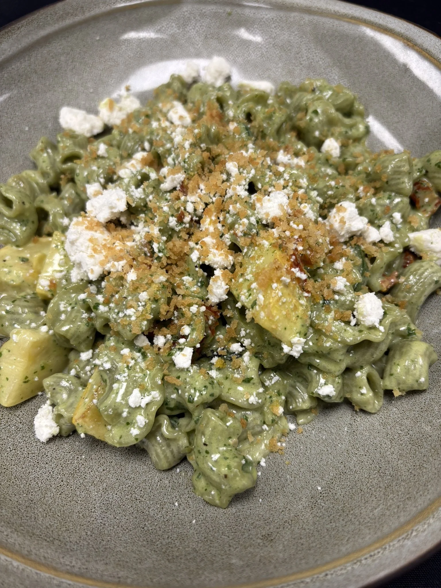 Creamy pasta salad with green herbs, topped with crumbled cheese and bread crumbs.