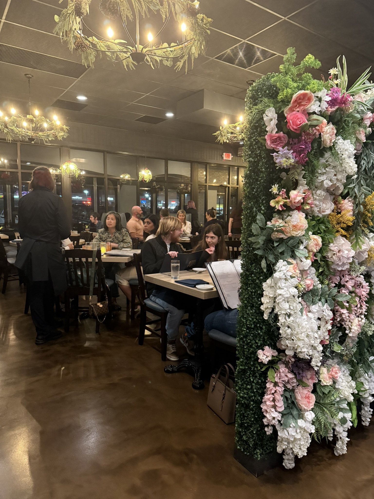 A lively restaurant with people dining and a floral decor pillar in the foreground.
