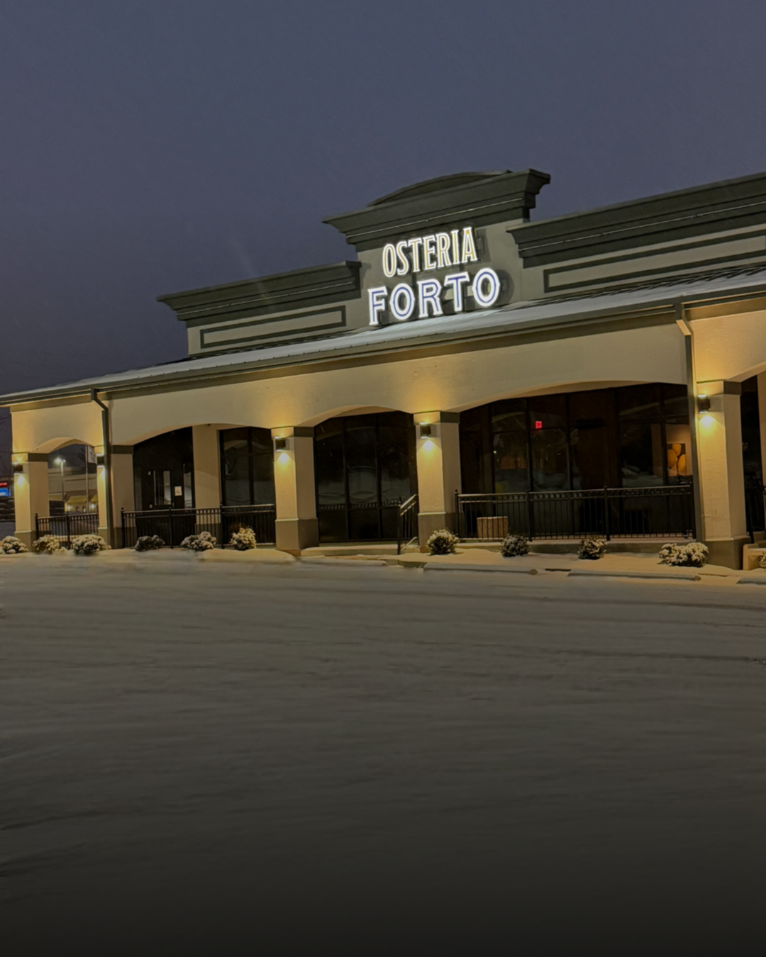 Night view of Osteria Forte restaurant with snow on the ground, illuminated sign, and decorated exterior.
