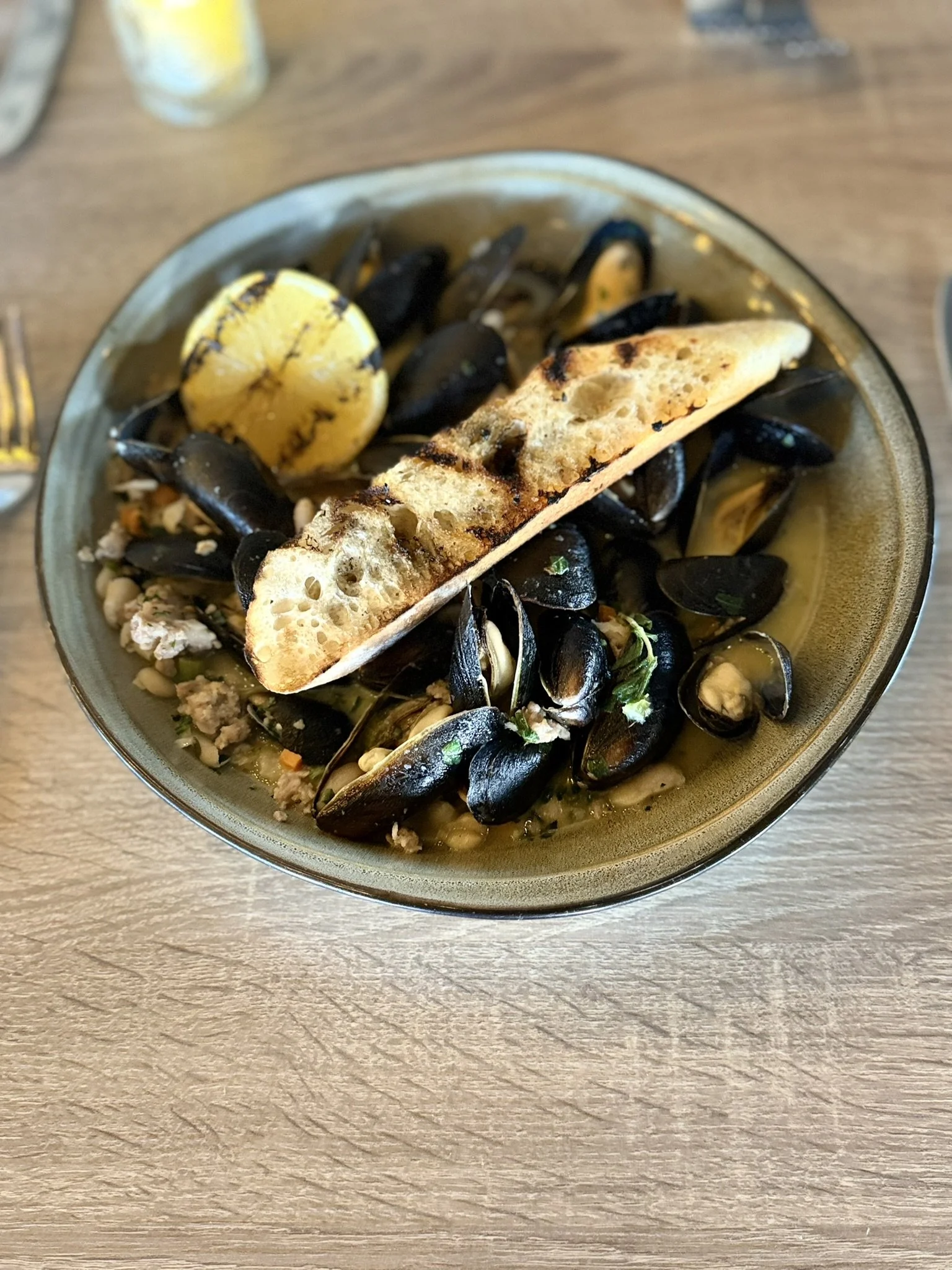 Bowl of steamed mussels with lemon wedge and toasted bread on top.
