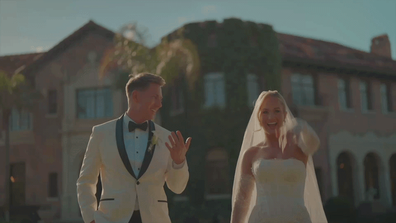A newlywed couple holding hands walks through falling confetti at their wedding reception.