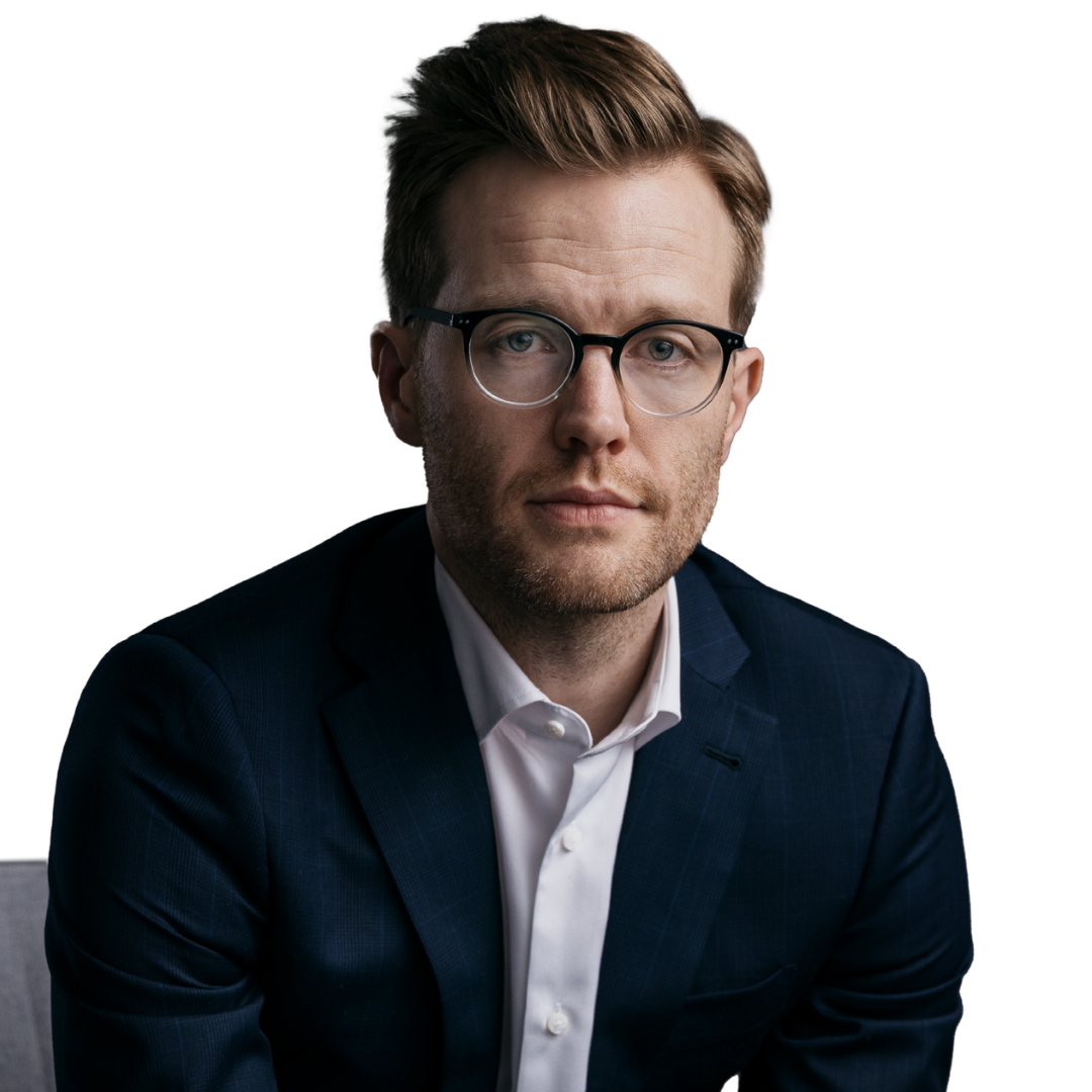 A man with glasses, wearing a dark suit and white shirt, poses for a portrait against a black background.
