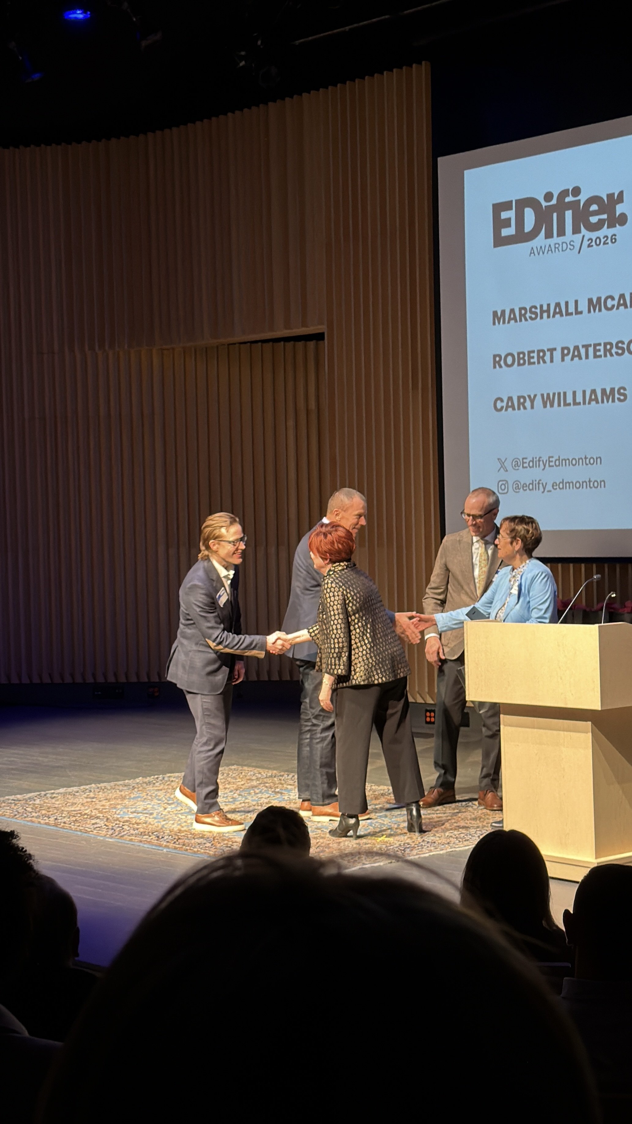 People on stage at an awards ceremony, with some shaking hands and others smiling. A large screen displays text and social media handles for Edifier Awards 2026.
