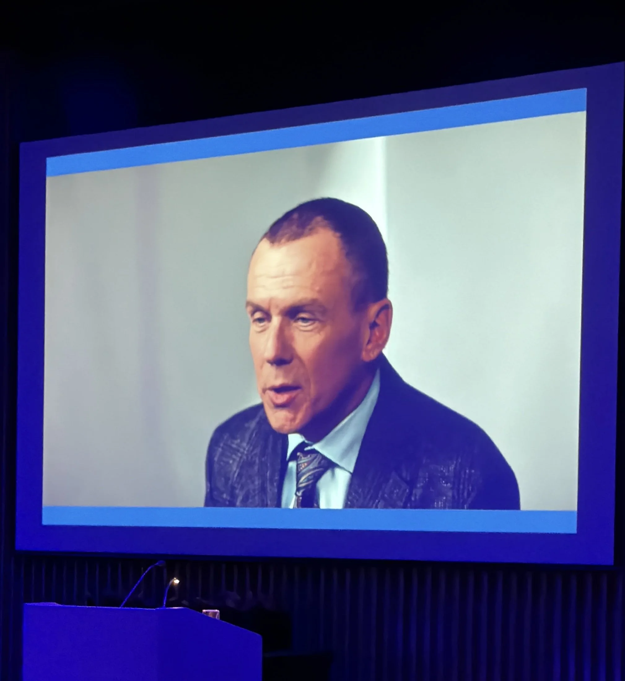 Projection screen displaying a close-up image of a man in formal attire with a dark background.