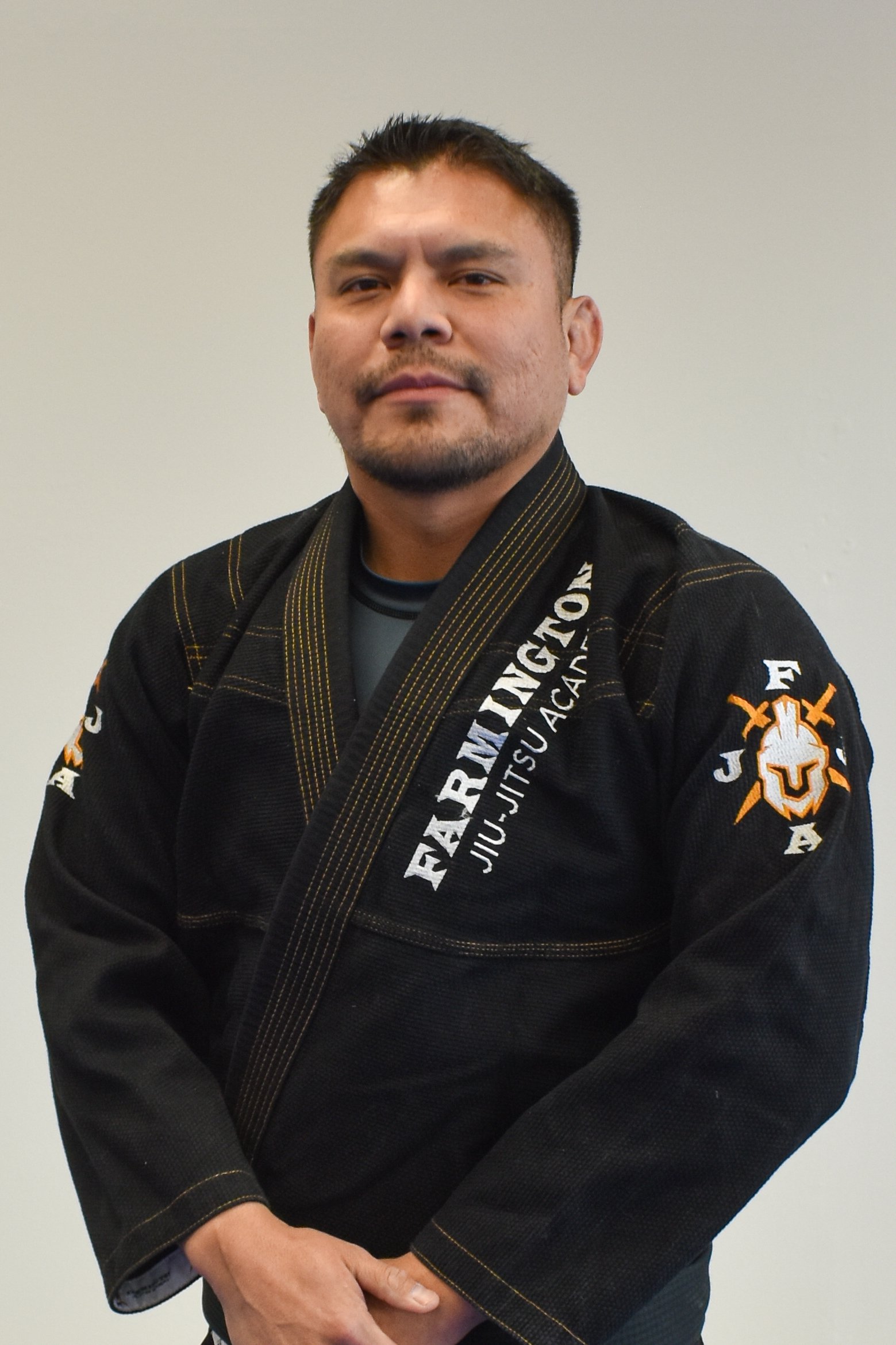 Professor Luke Harwood wearing a black Brazilian Jiu-Jitsu gi with yellow and white embroidered patches.