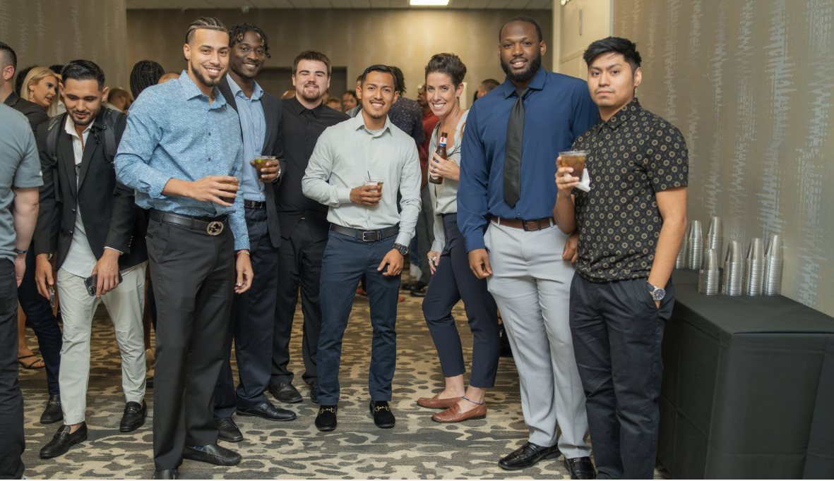 A diverse group of people at a professional social event, smiling and holding drinks, standing in a line.