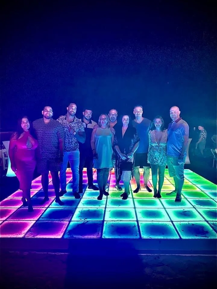 Group of people dancing on a colorful LED-lit dance floor at night.