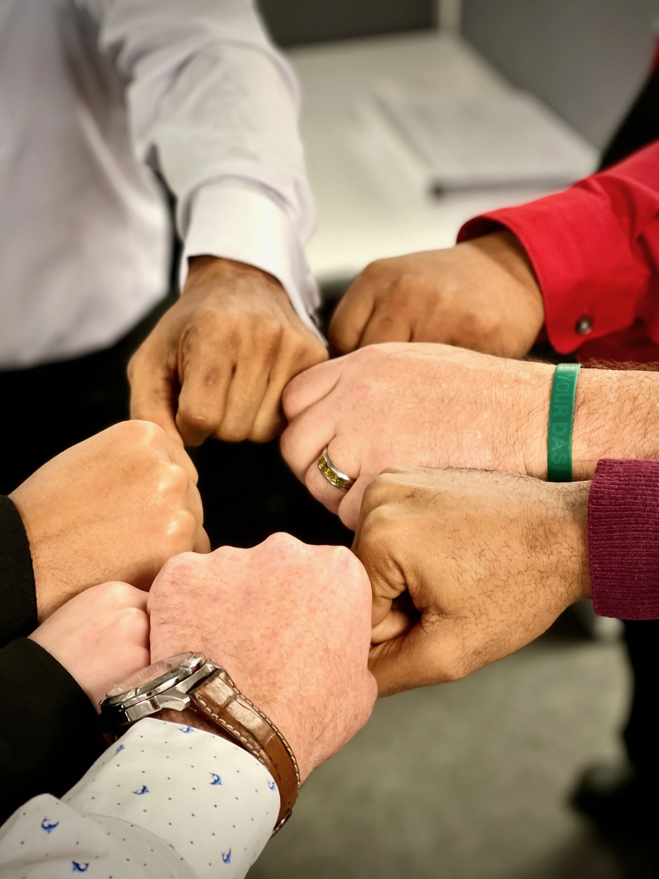 Multiple hands of diverse individuals joined together in a circle, showing unity and teamwork.