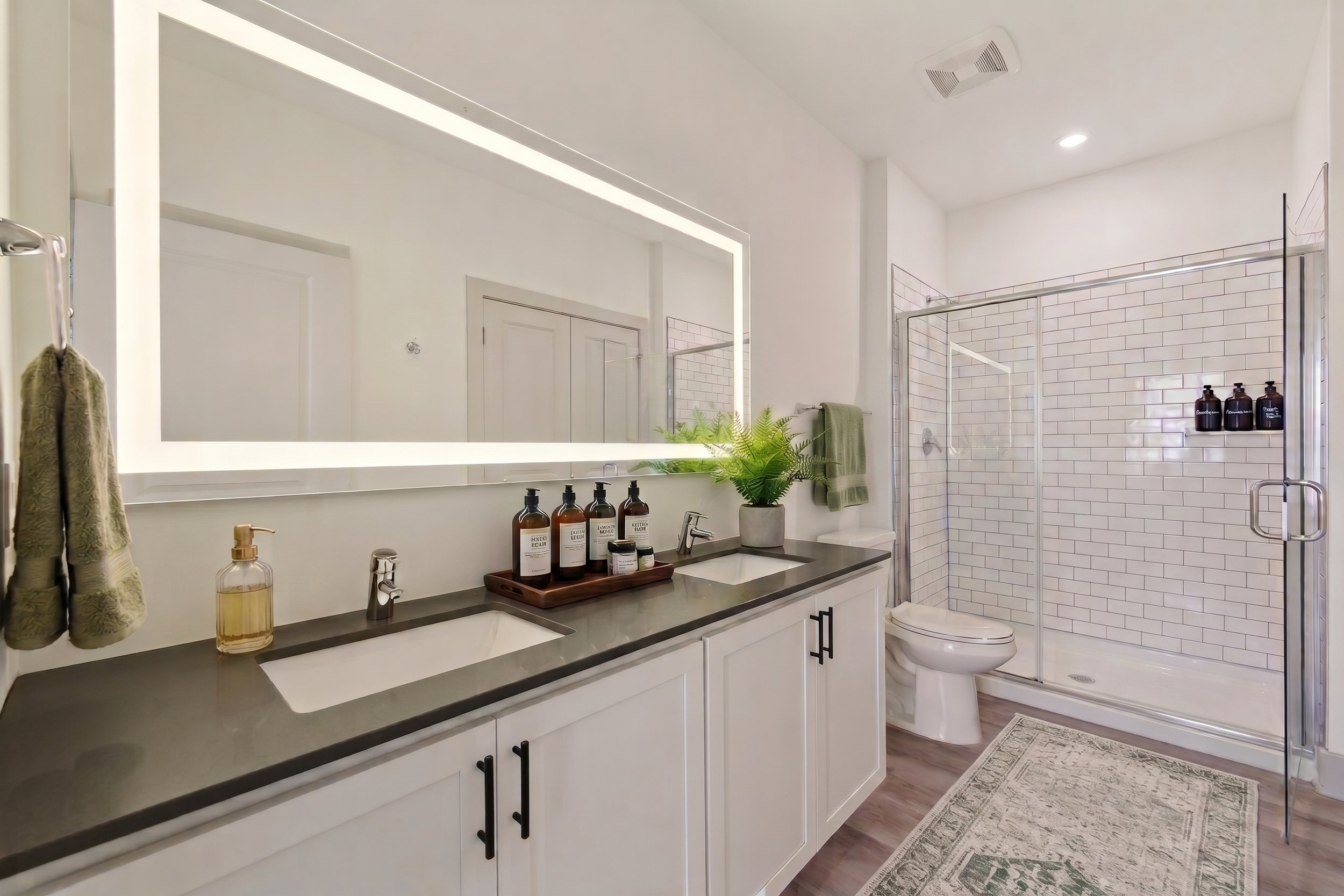 Modern bathroom with white cabinetry, black countertop, large mirror, small plant, and a glass-enclosed shower with white subway tile walls.