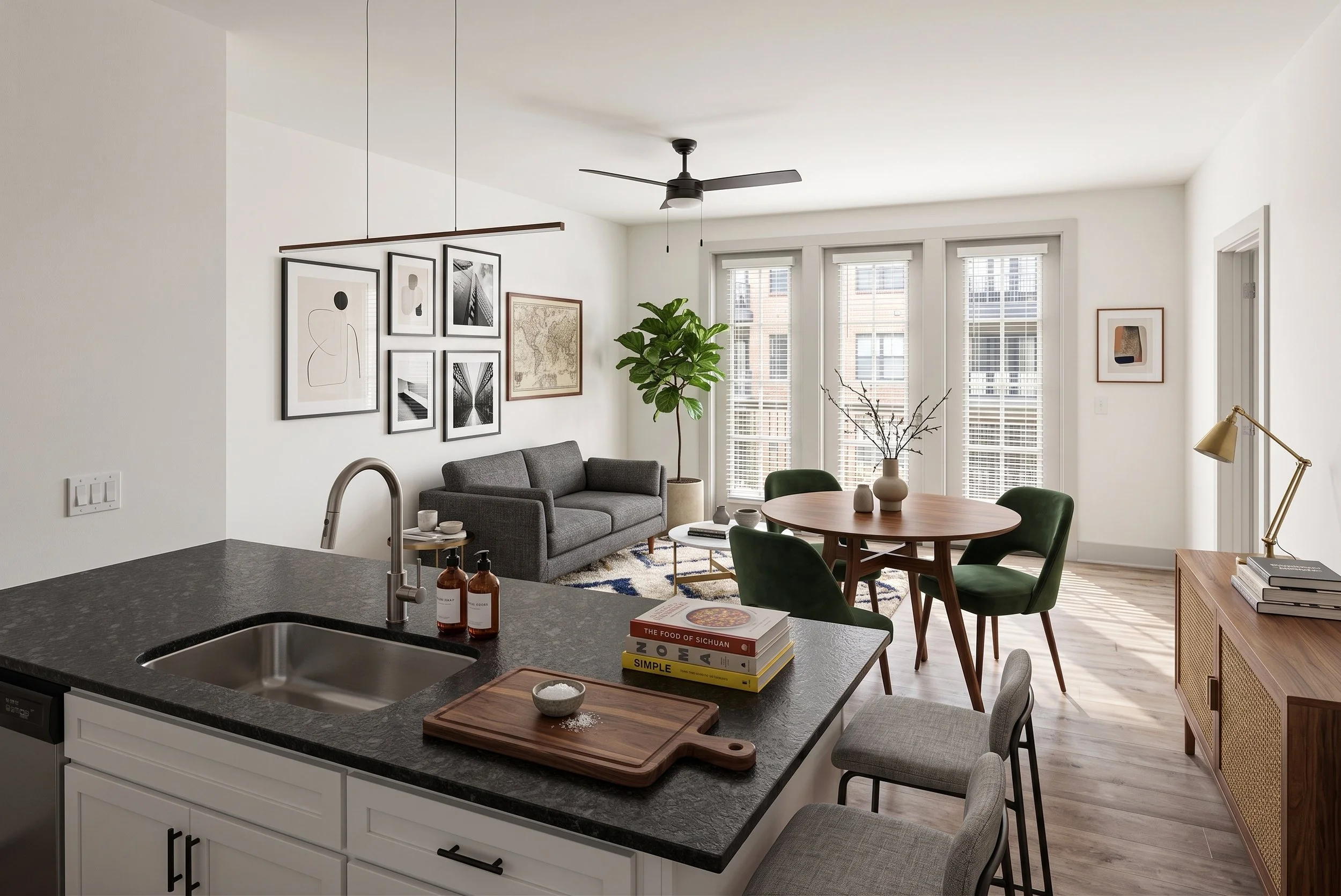 Open concept living room and kitchen with modern decor, gray sofa, framed wall art, large windows with blinds, potted plant, round dining table with green chairs, ceiling fan, and a bookshelf with books.