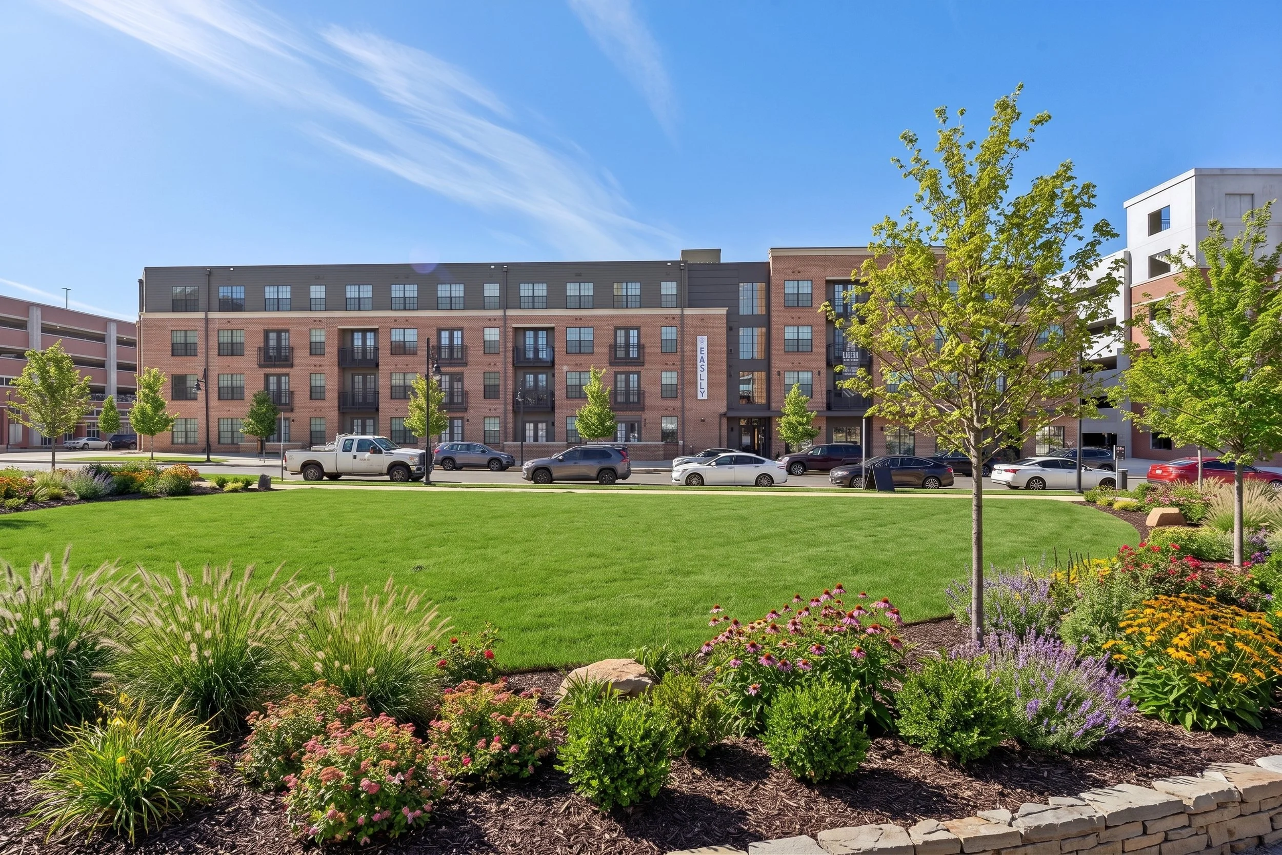 Bright sunny day in a University Center Rock Hill, SC with a beautiful flower garden, green grass, trees, and a modern apartment building in the background.