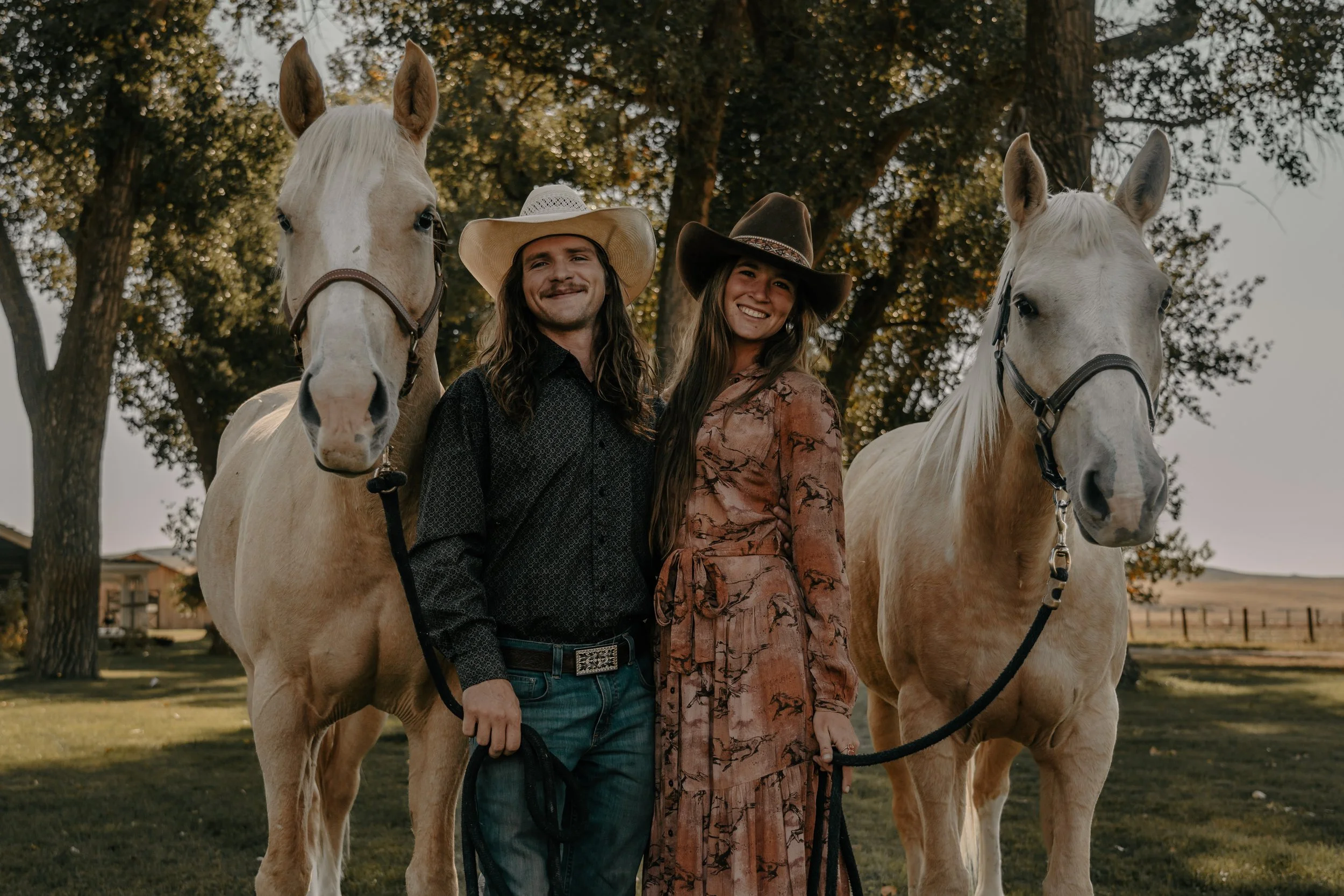 Tucker Giles and Tori Templin standing with their horses Cowboy and Billy in the Grove at the TA Ranch just outside of Buffalo, Wyoming. Dressed in fine clothes with cowboy hats and boots.