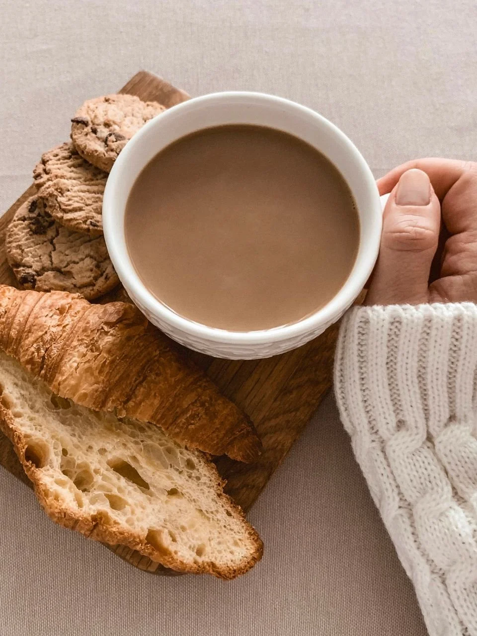Hands holding a cup of coffee next to fresh pastries