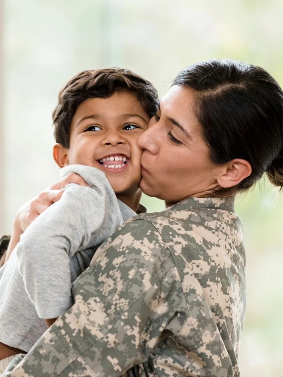 Service member in uniform kissing her young son