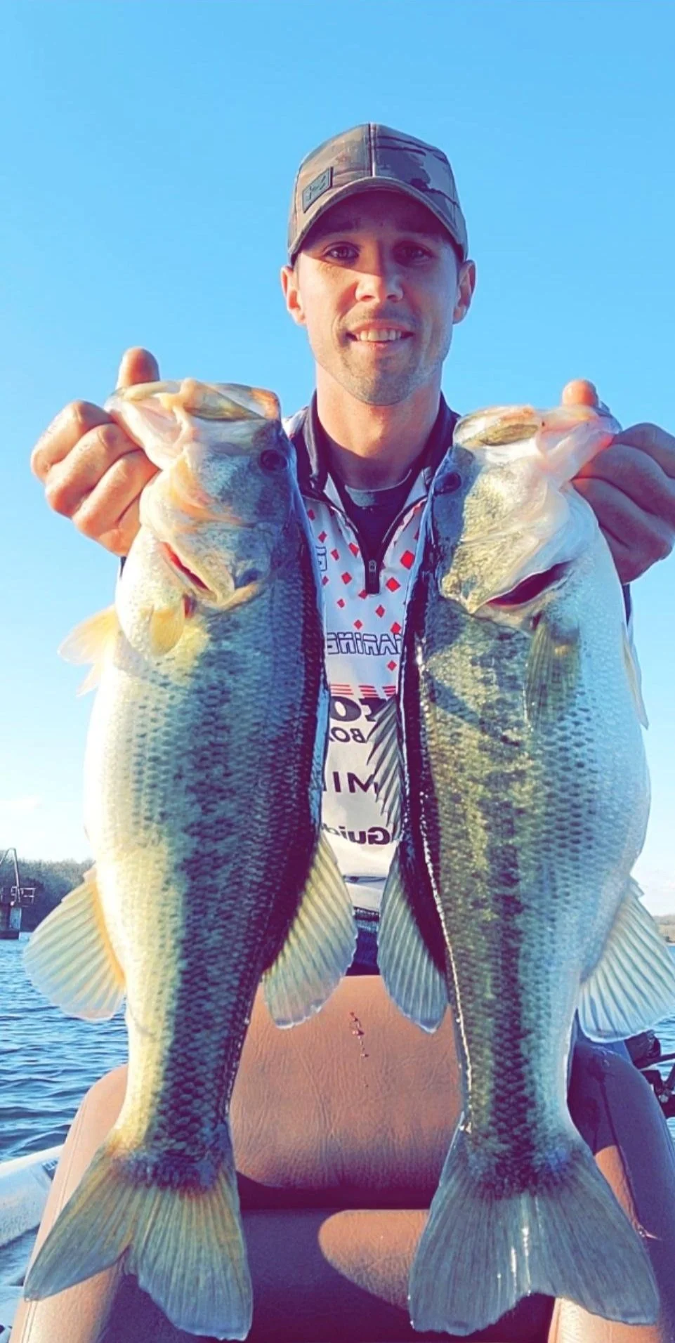 Person holding two large fish on a boat with blue sky background.