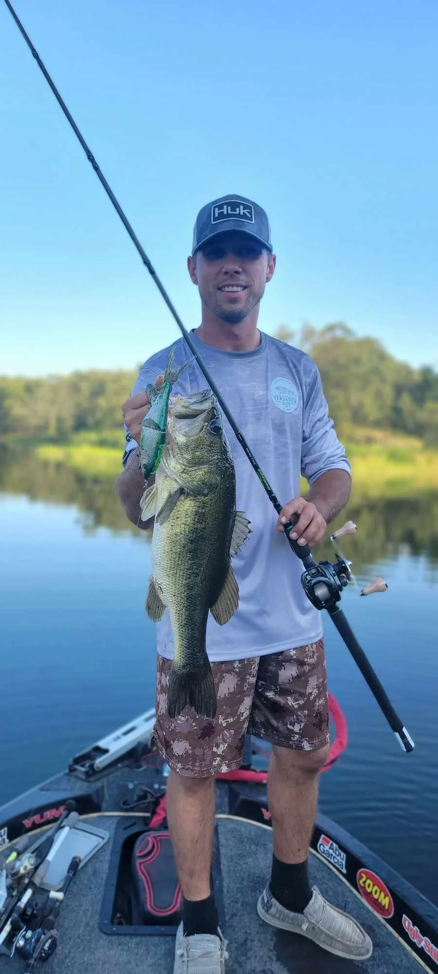 Person holding a largemouth bass and fishing rod on a boat in a lake.
