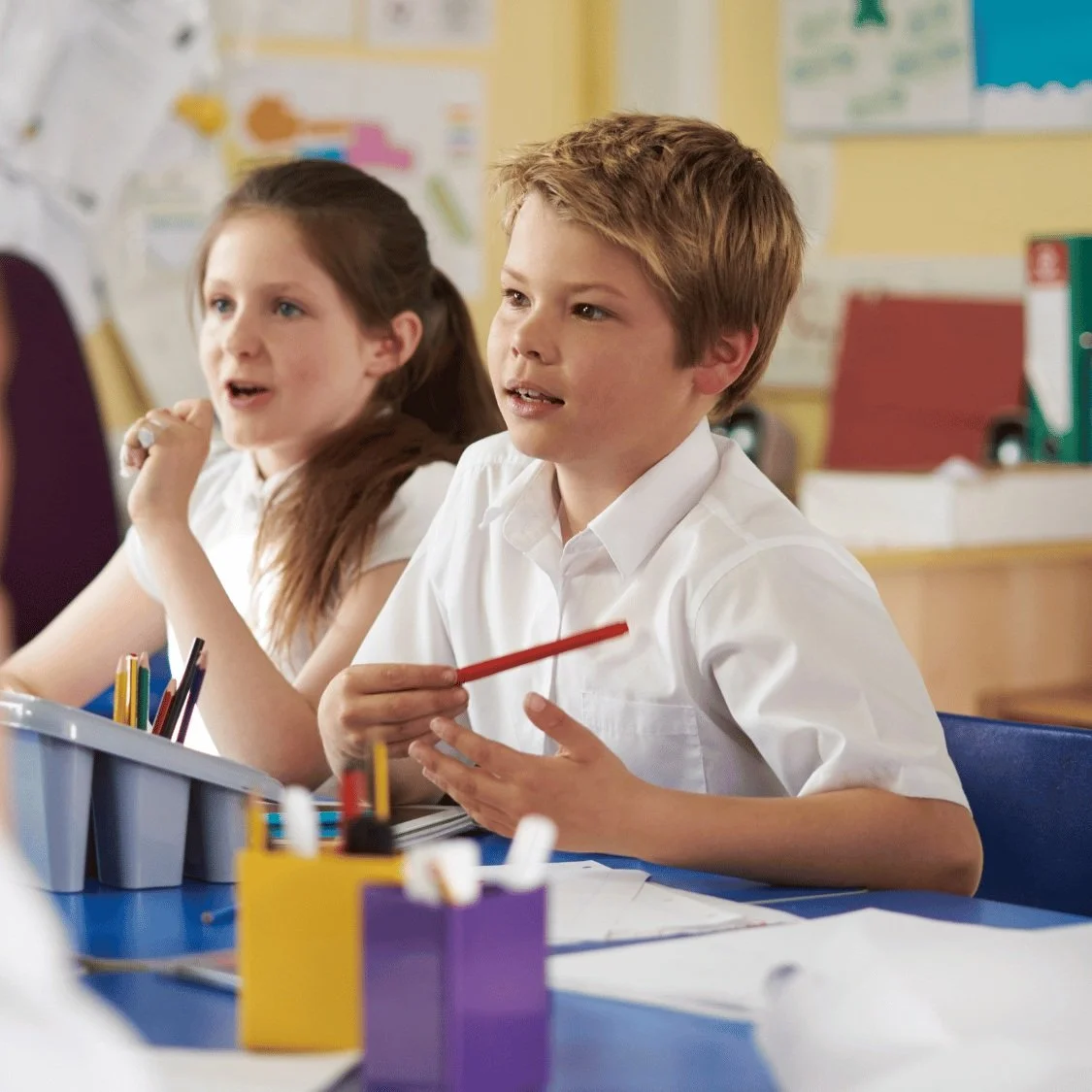 Close up of a young boy and girl student asking questions in their classroom while sitting at their desk.
