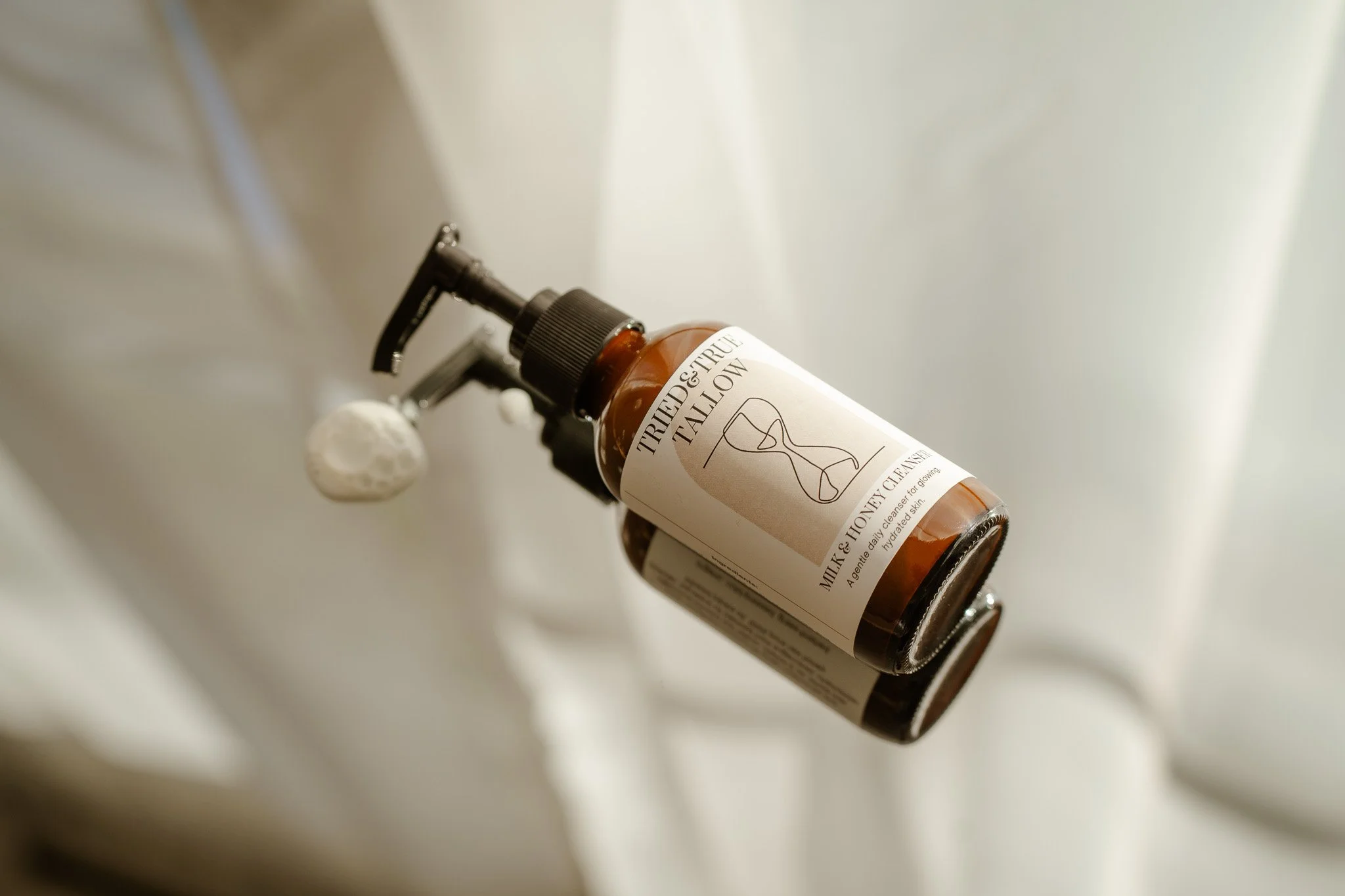 A small amber glass bottle with a pump dispenser labeled 'TRIED & TRUE TALLOW,' 'Milk & Honey Cleanse,' and 'Gentle daily cleanser for glowing, hydrated skin.'