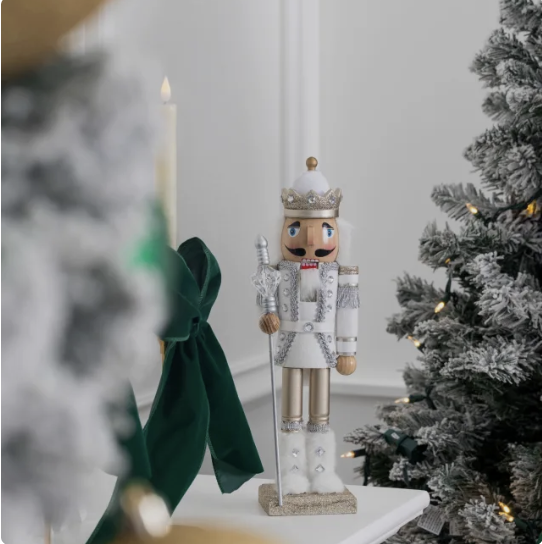 Decorative winter scene with a figurine of a toy soldier, Christmas tree with snow-like frosted branches, and a lit candle in the background.