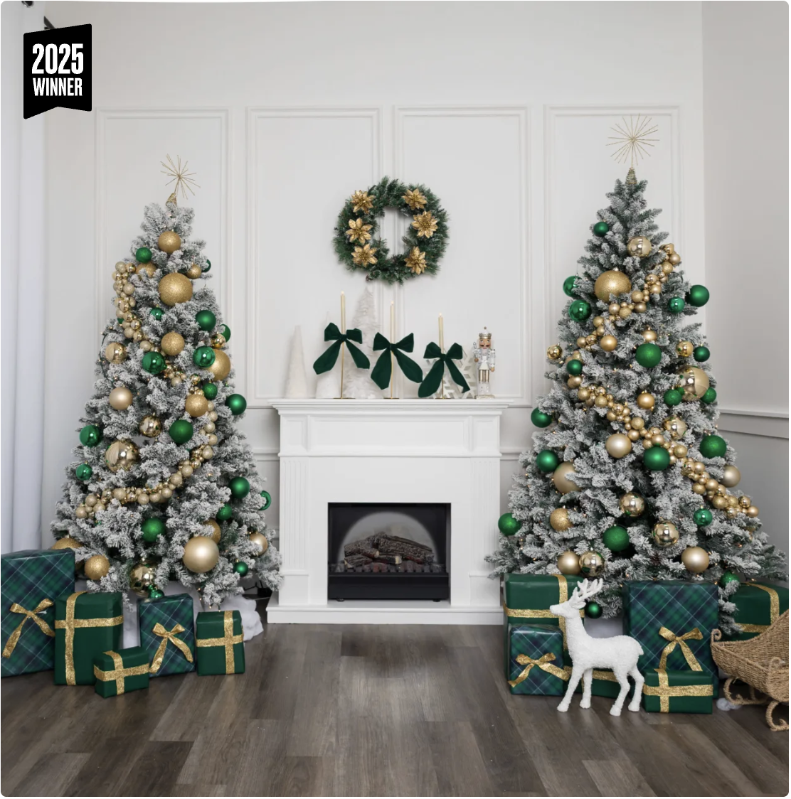 Christmas decorated living room with two snow-flocked Christmas trees decorated in gold and green ornaments, surrounded by wrapped gifts, a white fireplace with green bows, a holiday wreath, and holiday figurines.