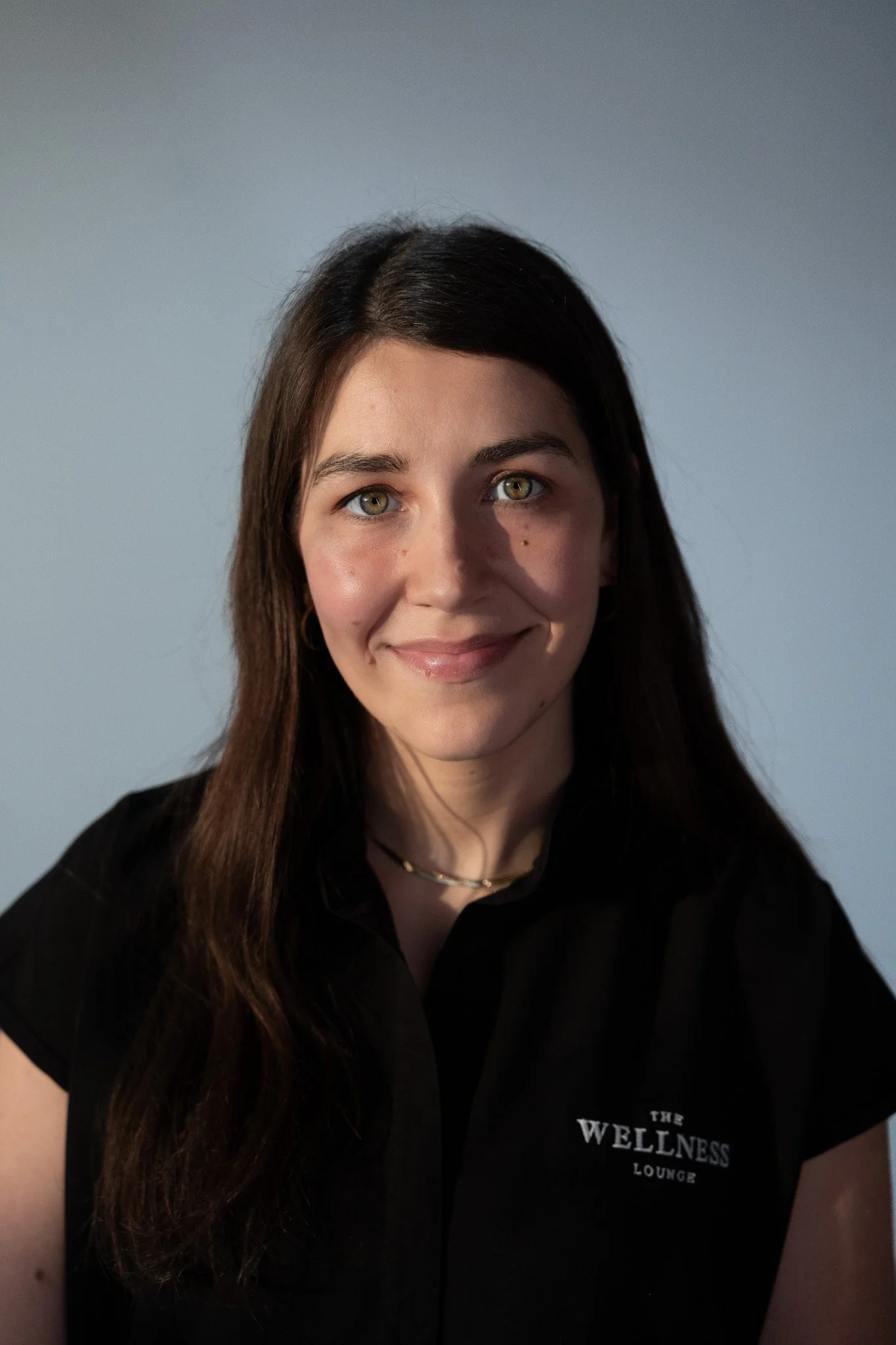 A young woman with long, wavy brown hair smiling and wearing a black shirt.