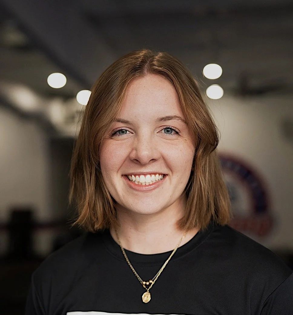 Headshot style photo: White female with short dirty blonde hair in a  bob cut. She is wearing a black t shirt and a gold chain necklace.