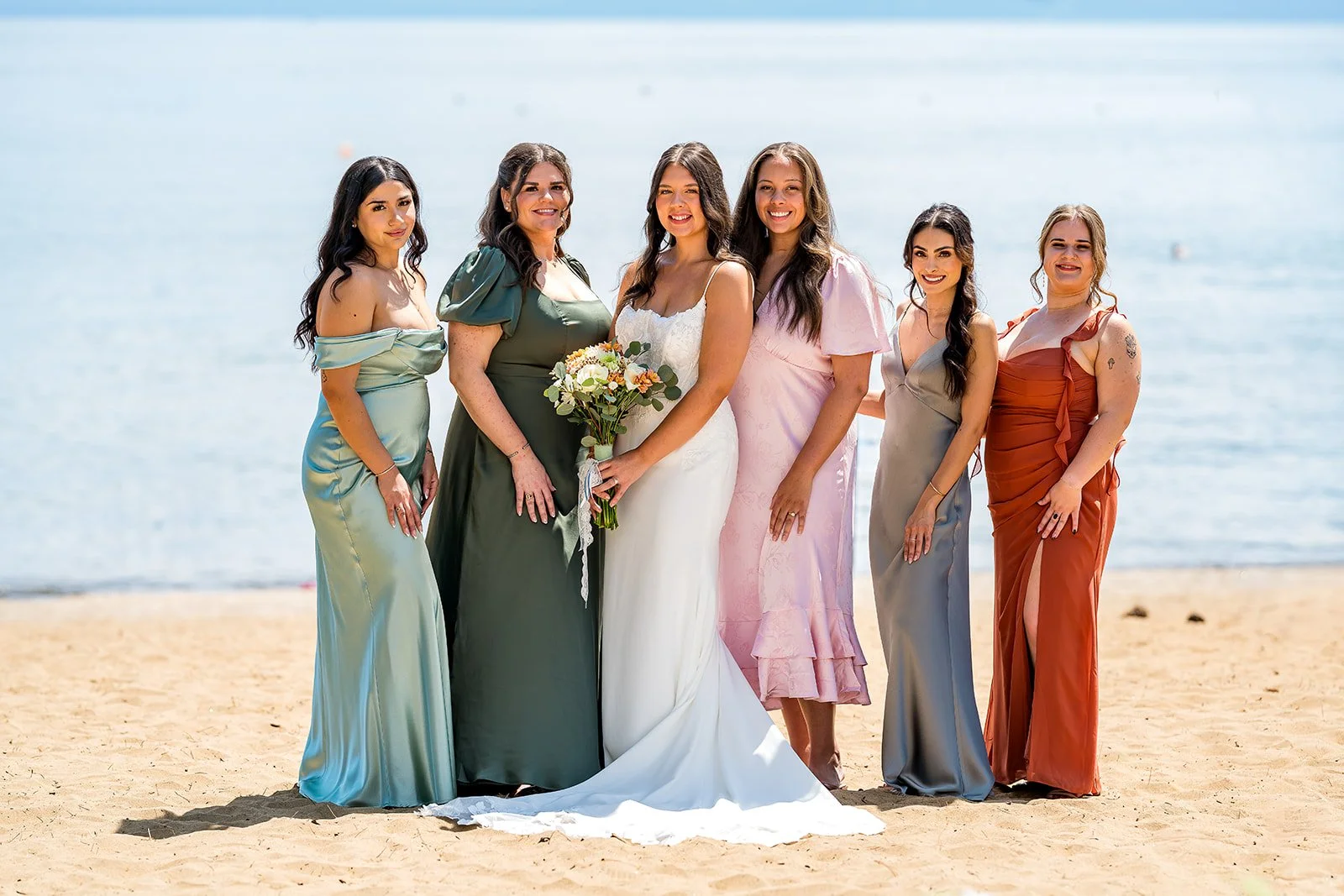  A bride stands with her bridesmaids wearing dresses of various colors with Lake Tahoe in the background at the North Tahoe Event Center in Kings  Beach, California. 