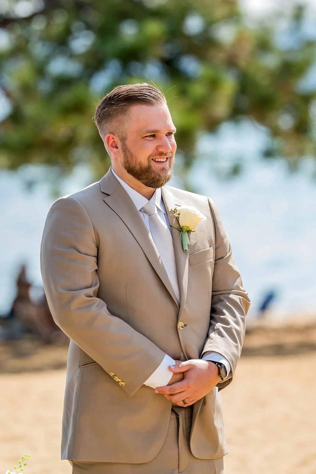  A groom in a tan suit smiles at his wedding ceremony with Lake Tahoe in the background at the North Tahoe Event Center in Kings  Beach, California. 