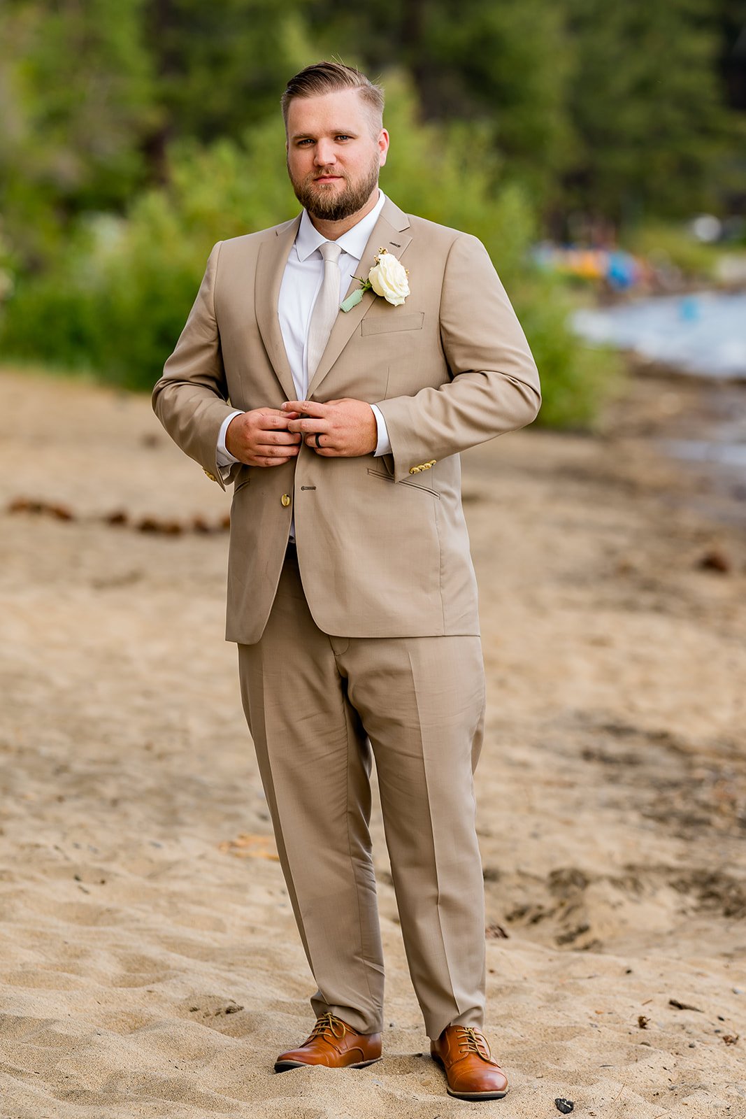  A groom in a tan suit looks at the camera with Lake Tahoe in the background at the North Tahoe Event Center in Kings  Beach, California. 